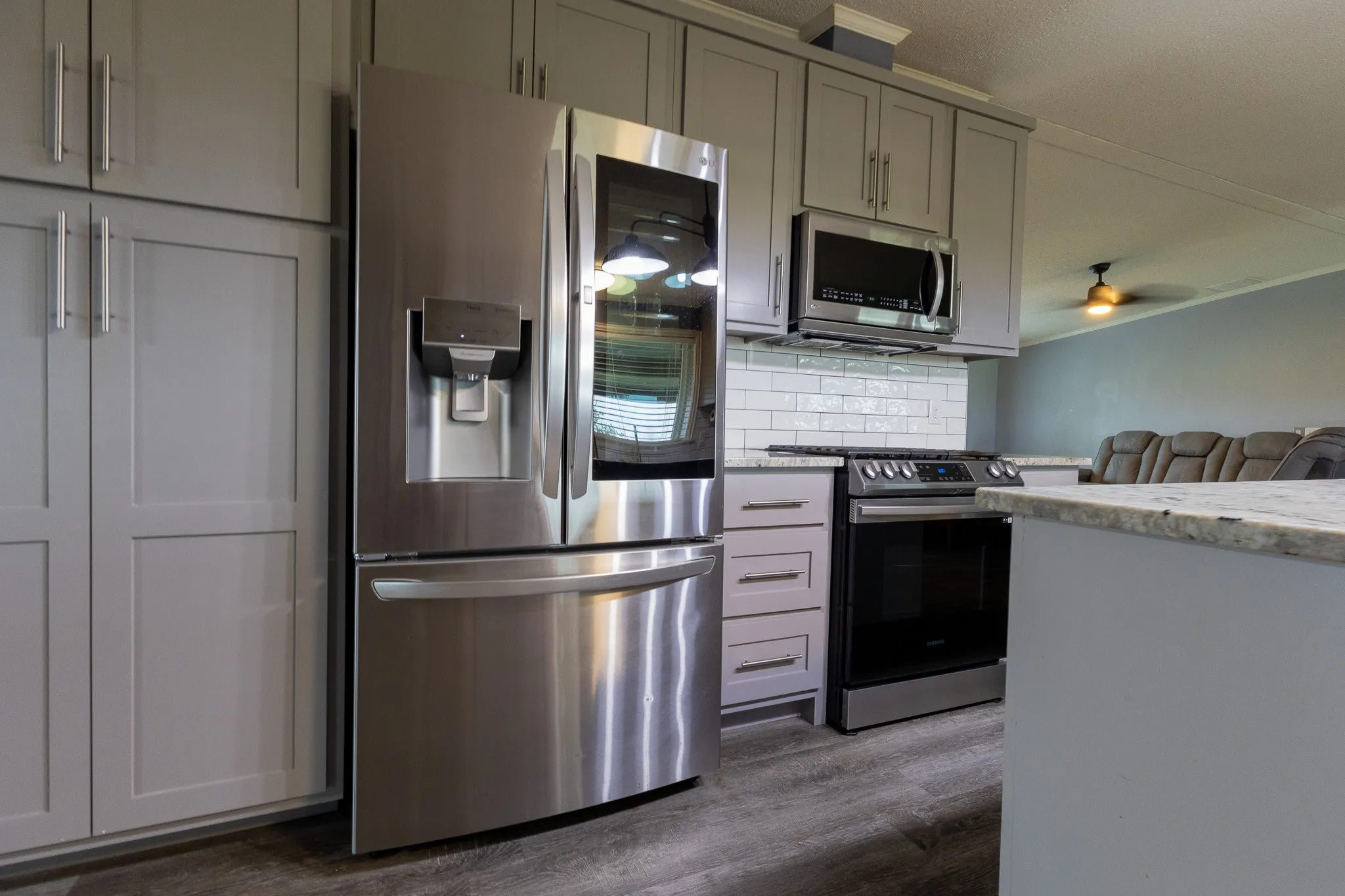 Kitchen featuring stainless steel appliances, grey shaker-style cabinetry, wood-finish flooring, white subway tile backsplash, and light-toned countertops