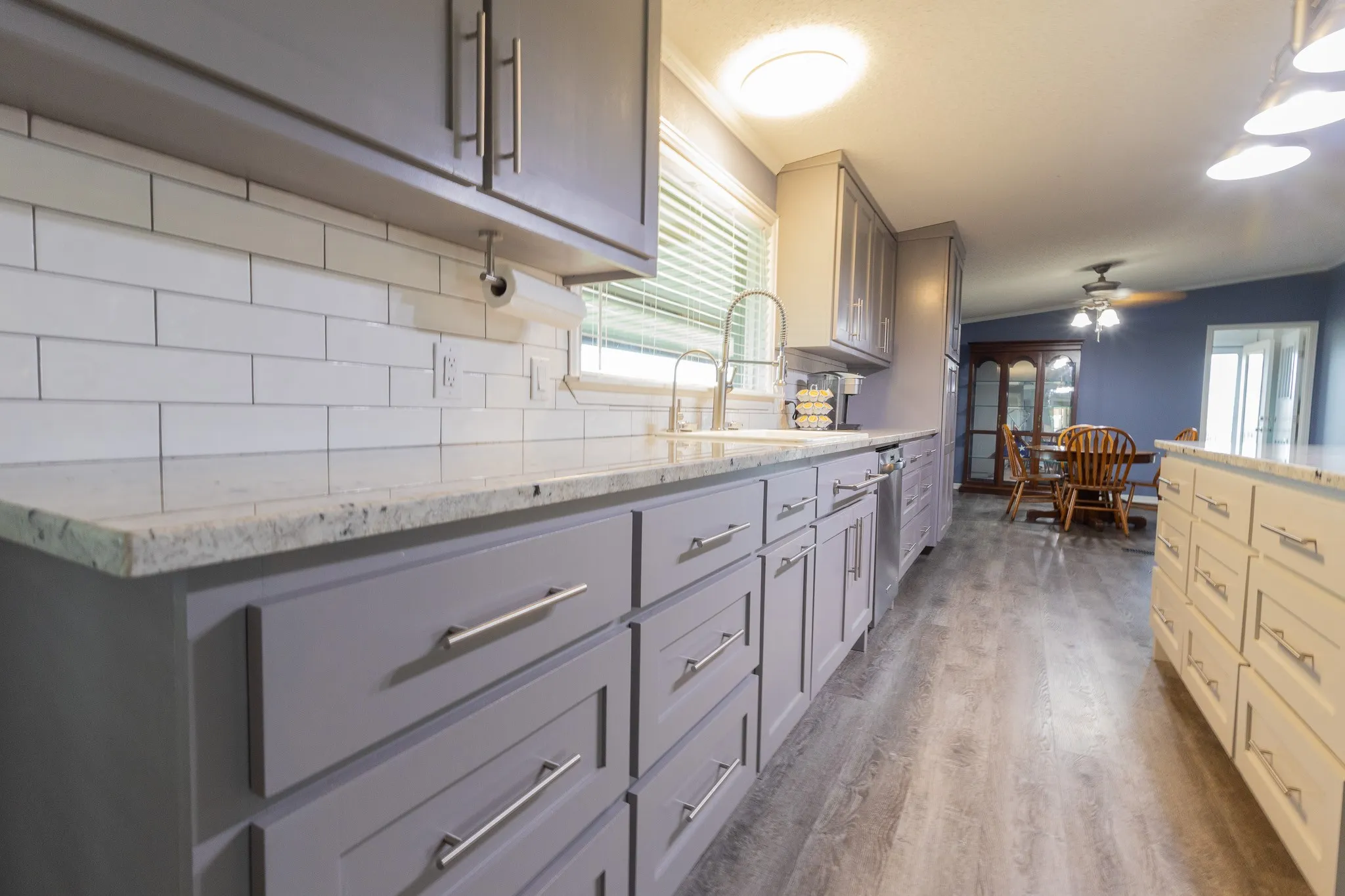 Kitchen featuring wood-finish flooring, gray lower cabinetry with contemporary hardware, white subway tile backsplash, and light-toned countertops