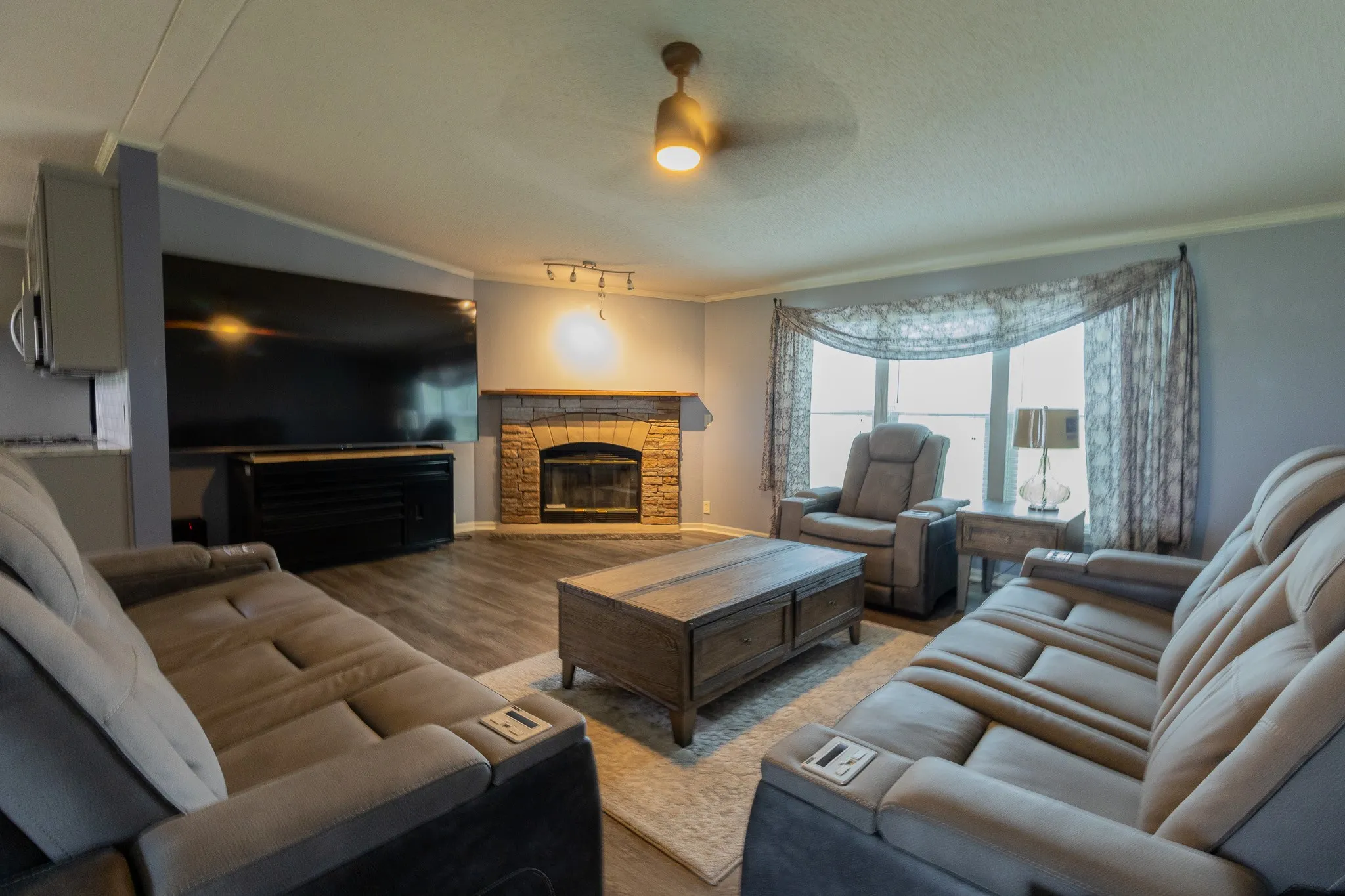Living area featuring a stone-clad fireplace with hearth, wood-finish flooring, and a ceiling fan with light fixture