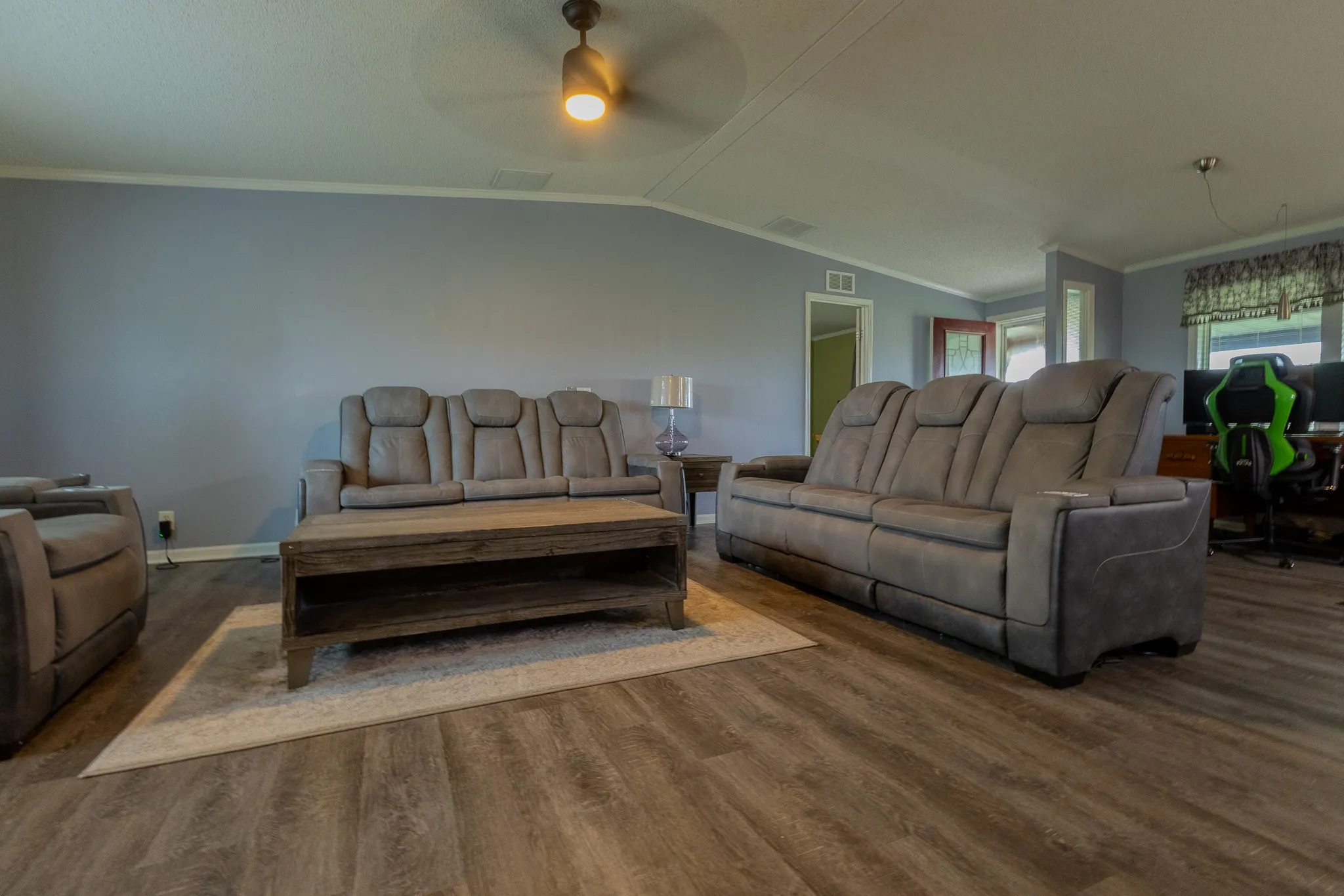 Spacious living area featuring wood-finish flooring, a ceiling fan with integrated lighting, and crown molding
