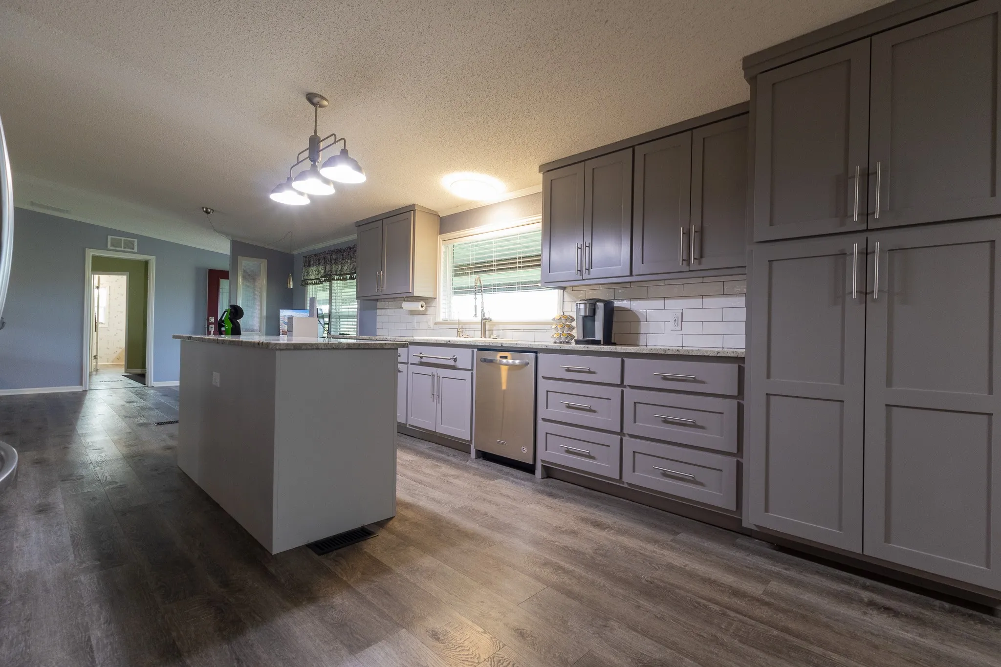 Kitchen featuring wood-finish flooring, an island with countertop, grey cabinetry, stainless steel dishwasher, and a white subway tile backsplash