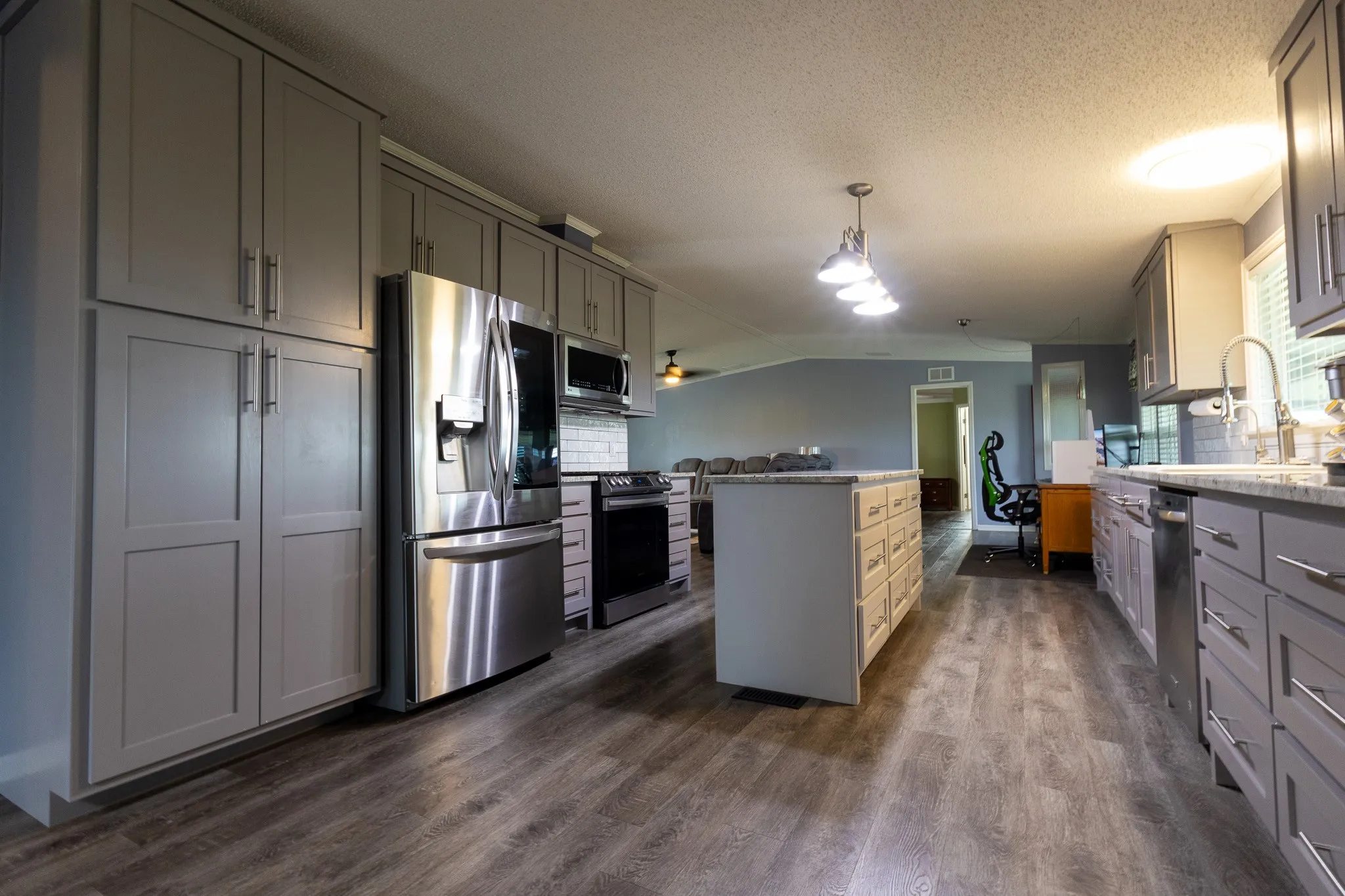Contemporary kitchen featuring wood-finish flooring, grey cabinetry with brushed nickel hardware, stainless steel appliances, a kitchen island with storage, and a pendant light fixture
