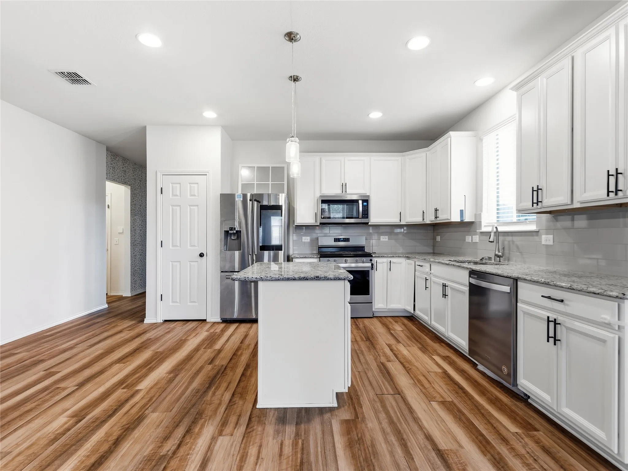 Contemporary kitchen featuring wood-finish flooring, white cabinetry with black hardware, stainless steel appliances, a center island, and recessed lighting
