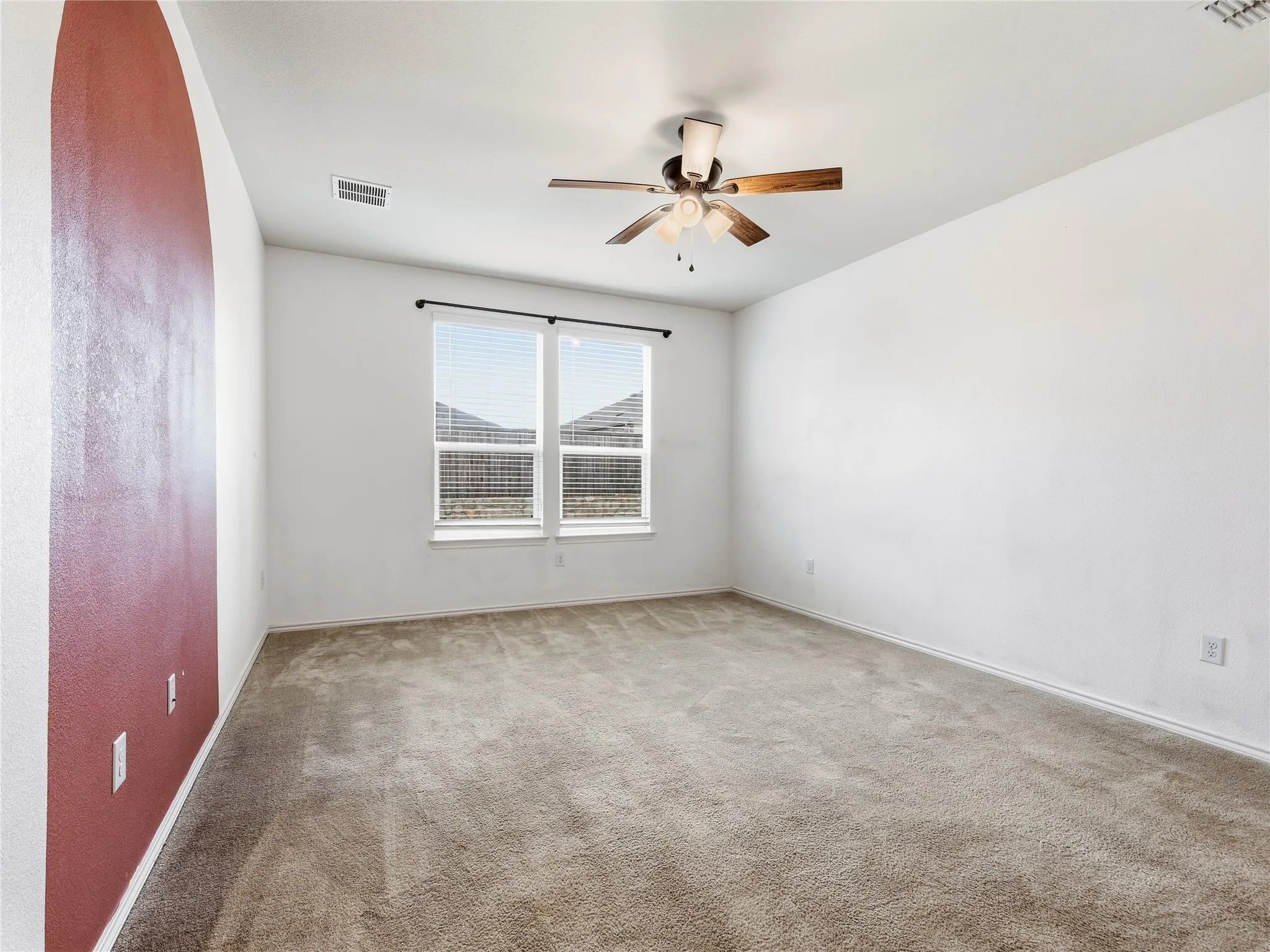 Spacious interior room featuring a neutral carpet flooring, white walls, and a ceiling fan with integrated lighting