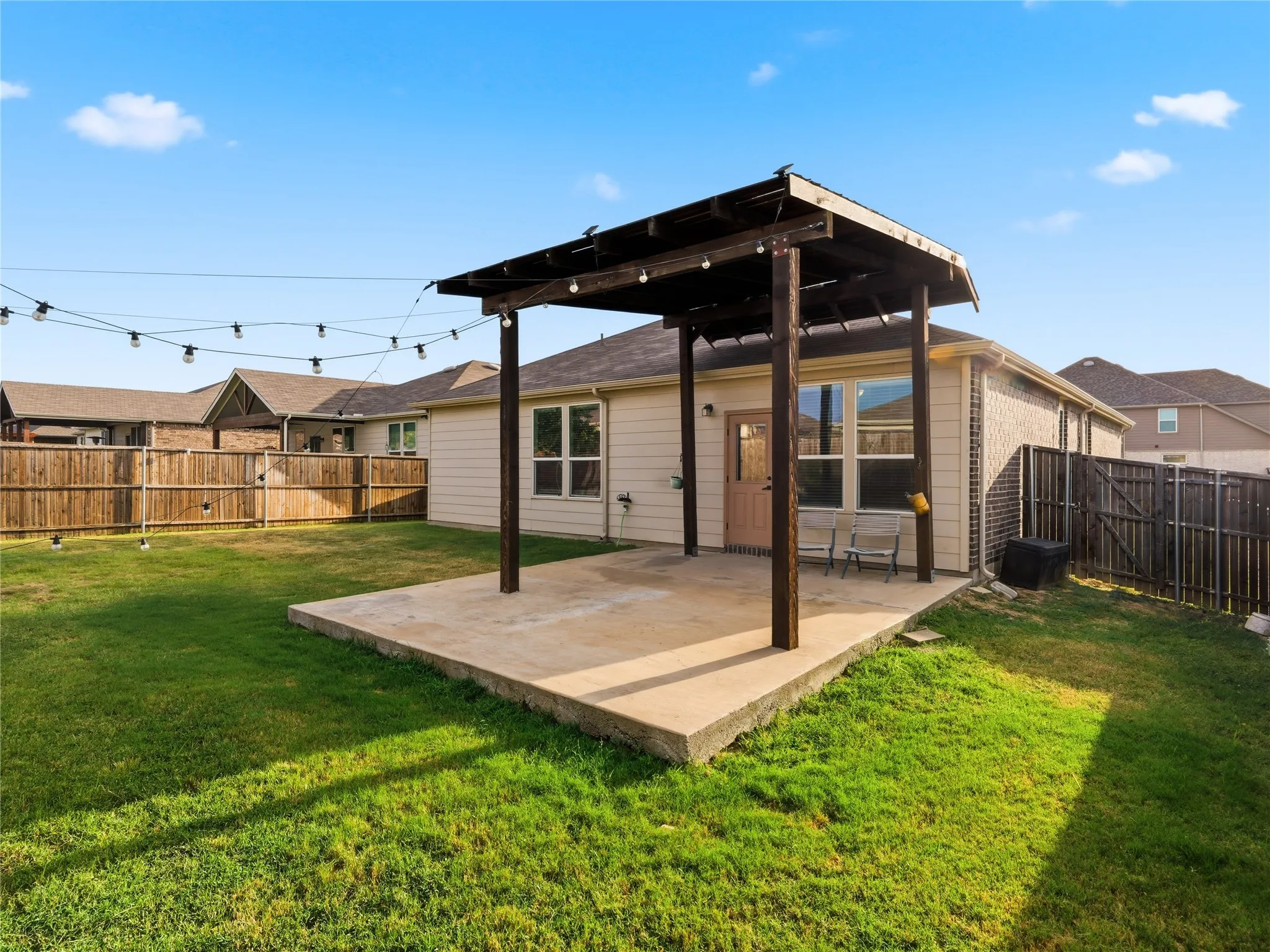 Expansive backyard featuring a concrete patio with a wooden pergola, string lighting, and a manicured lawn