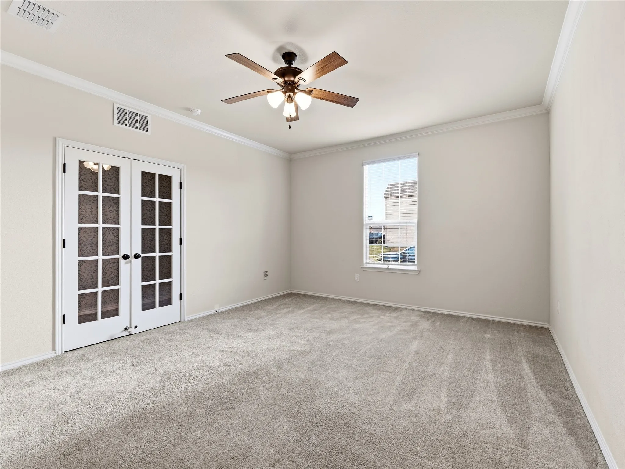 Spacious room featuring French doors with glass panes, a single window, a ceiling fan with light fixture, light gray carpet, and white crown molding