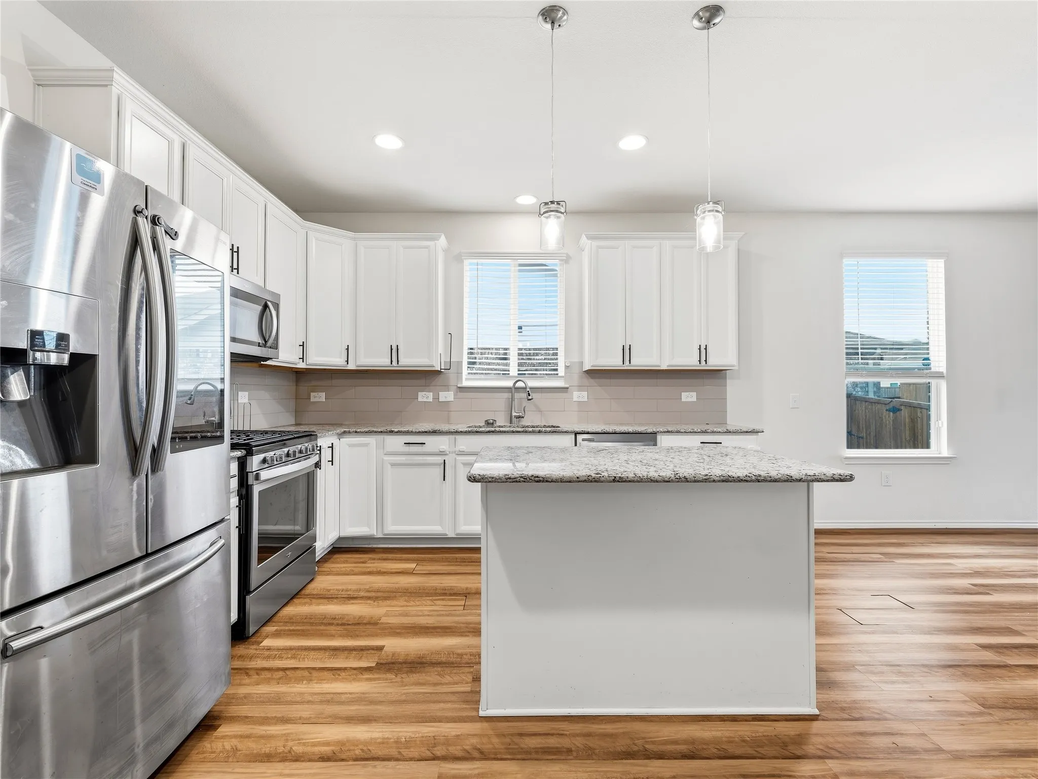 Spacious kitchen featuring white cabinetry, stainless steel appliances, wood-finish flooring, a central island with a granite countertop, and recessed lighting