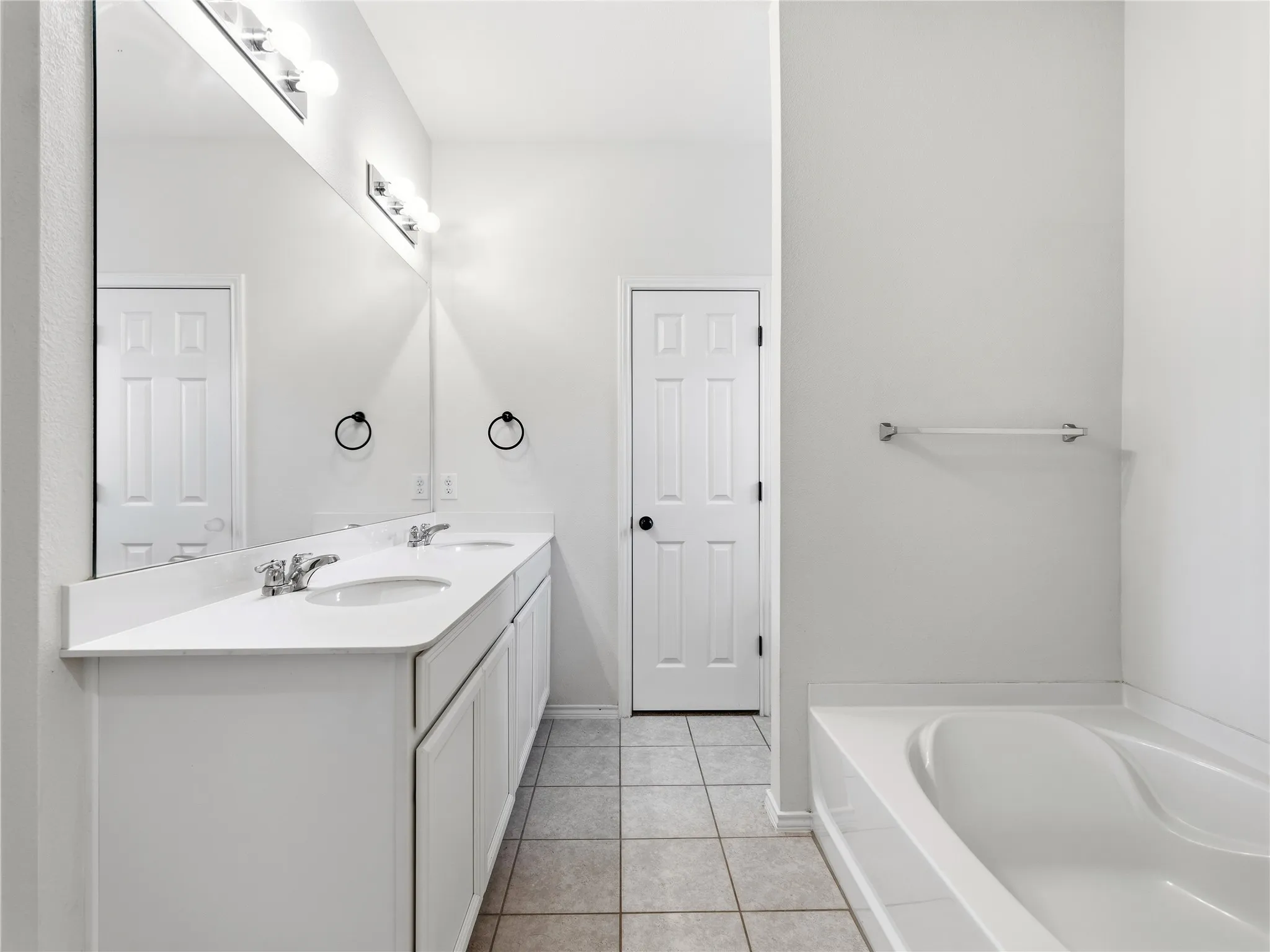 Bathroom featuring a dual vanity with integrated sinks and a white countertop, large wall-mounted mirror, and a built-in bathtub with white surround