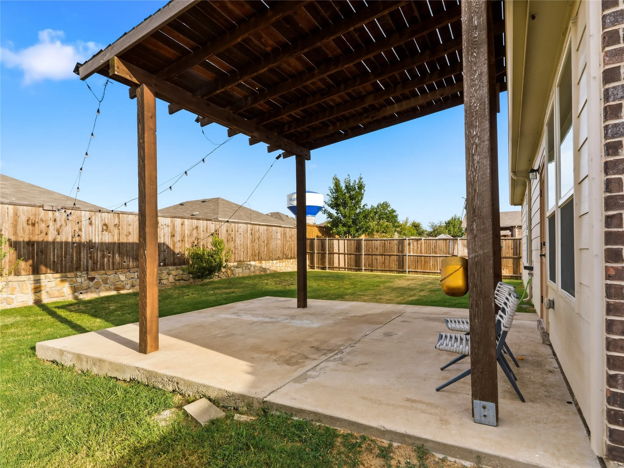 Spacious backyard patio featuring a wood pergola and concrete slab, surrounded by natural grass and a privacy fence