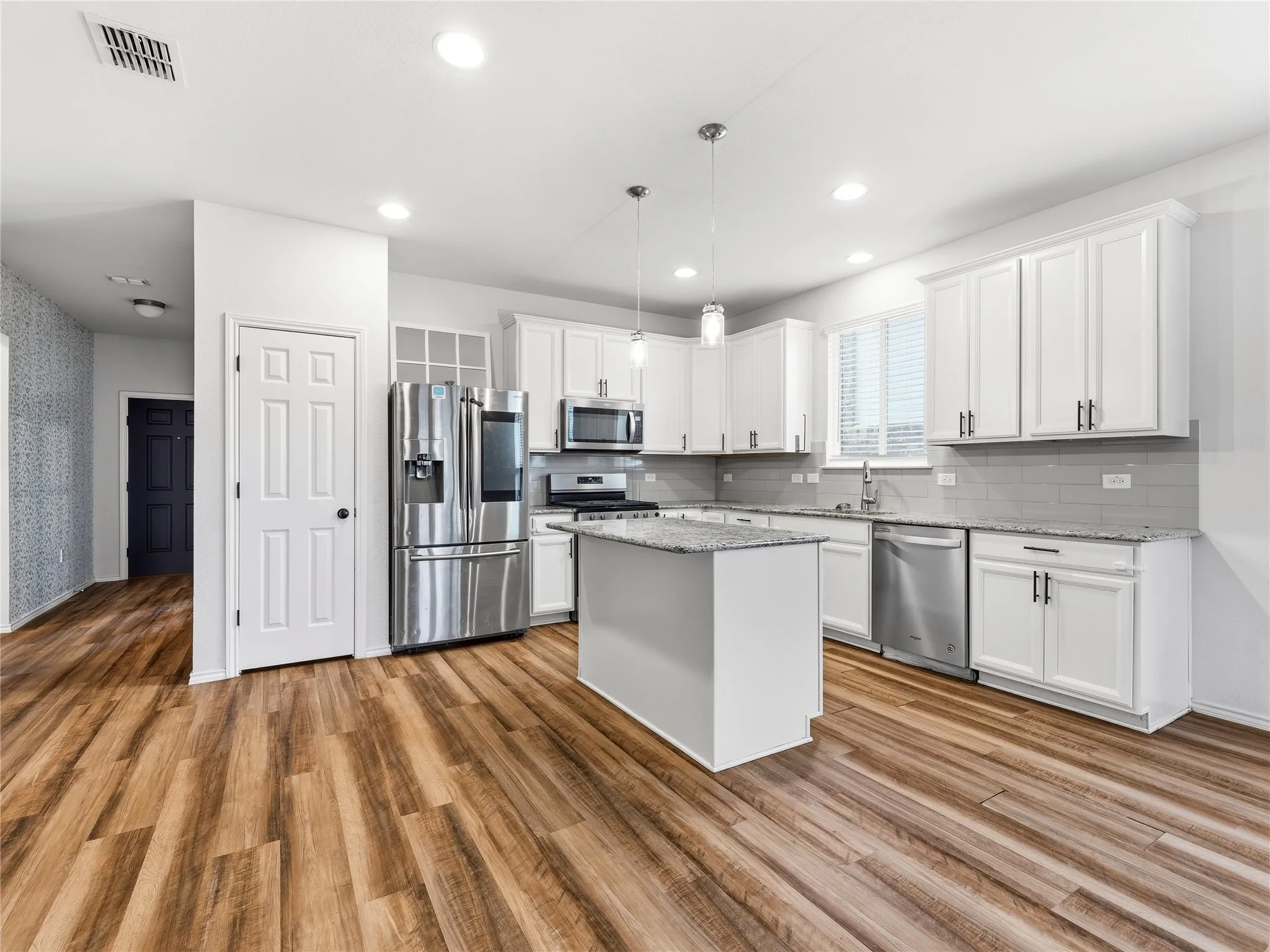 Bright kitchen with wood-finish flooring, white cabinetry, a central island, stainless steel appliances, and recessed lighting