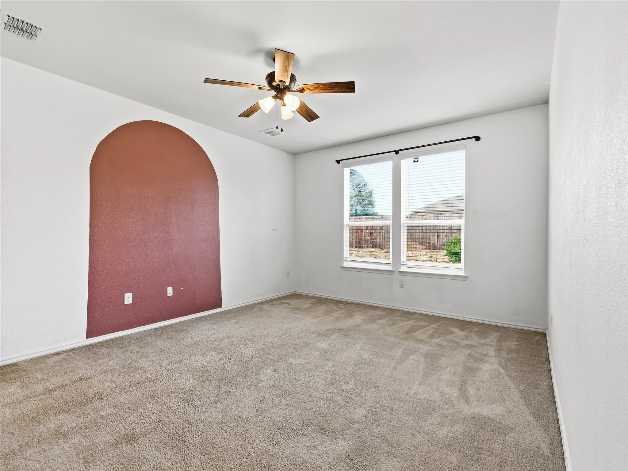 Spacious room featuring an arched accent wall, neutral carpeting, and a ceiling fan with integrated lighting