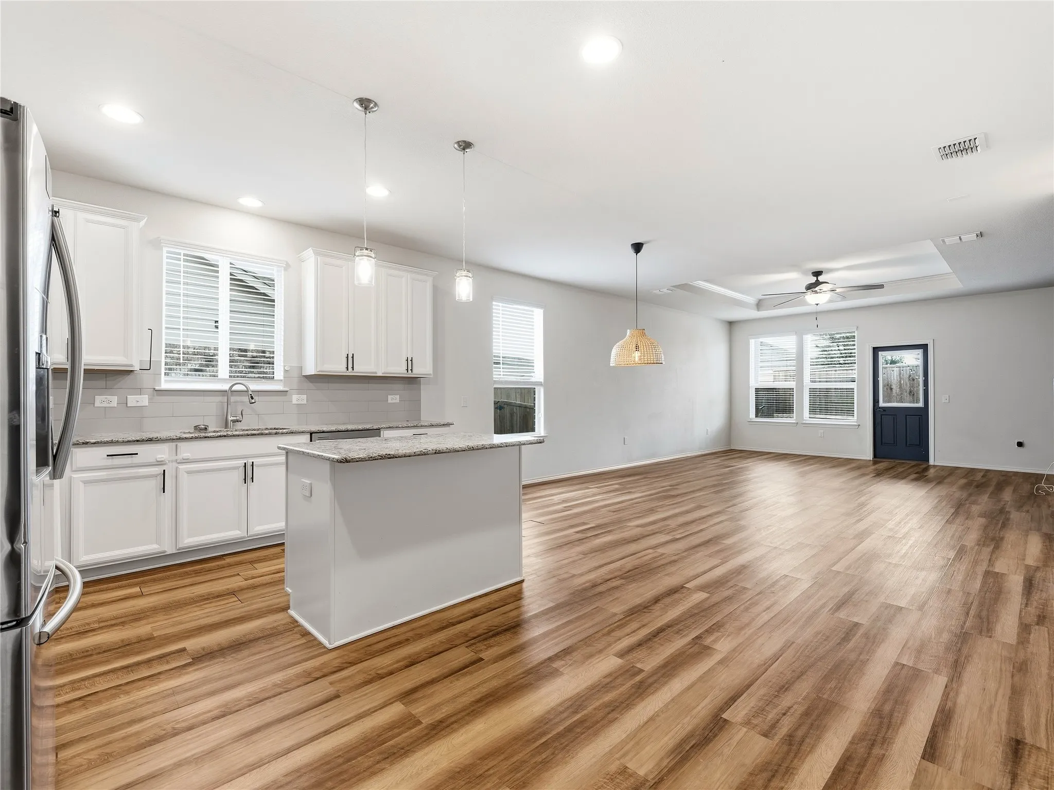 Open-concept interior featuring wood-finish flooring, a kitchen island with pendant lighting, white cabinetry, and stainless steel appliances