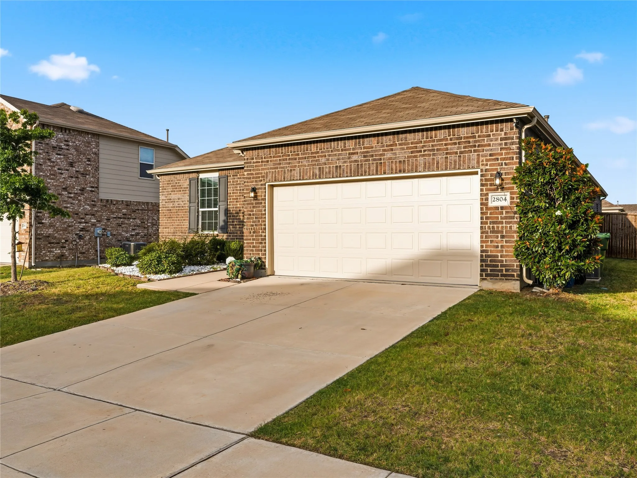 Brick exterior featuring a two-car garage, concrete driveway, and mature landscaping
