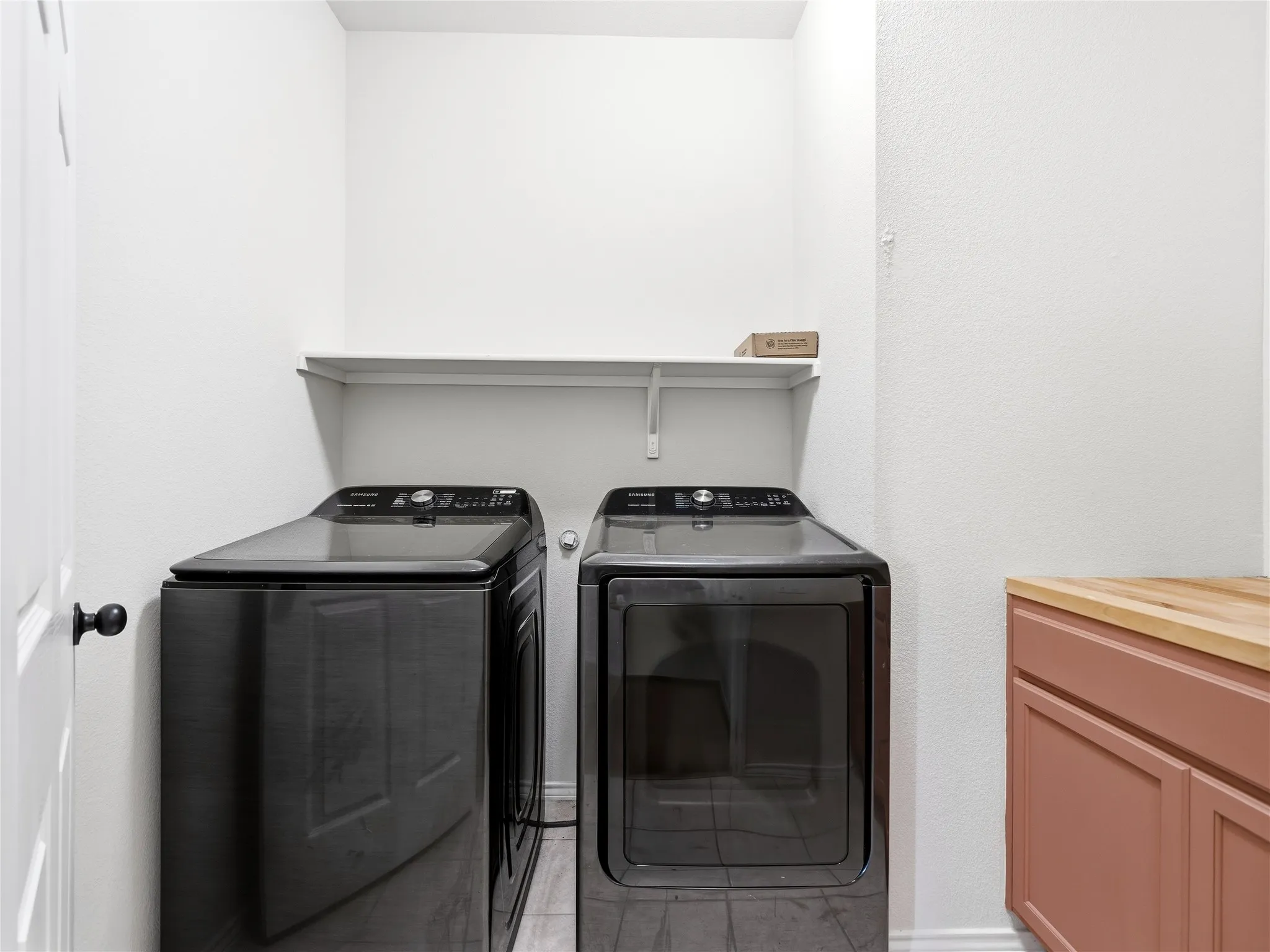 Laundry area featuring a light wood-finish countertop, pink cabinetry, and a white wall shelf