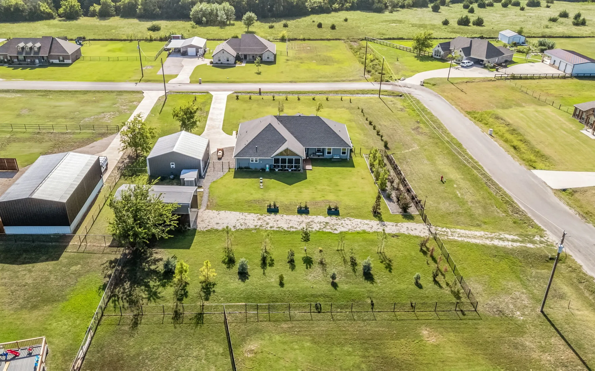 Aerial perspective showcasing home, a screened-in porch, Outbuildings, gated gravel drive to covered RV parking and wrought iron backyard fencing.