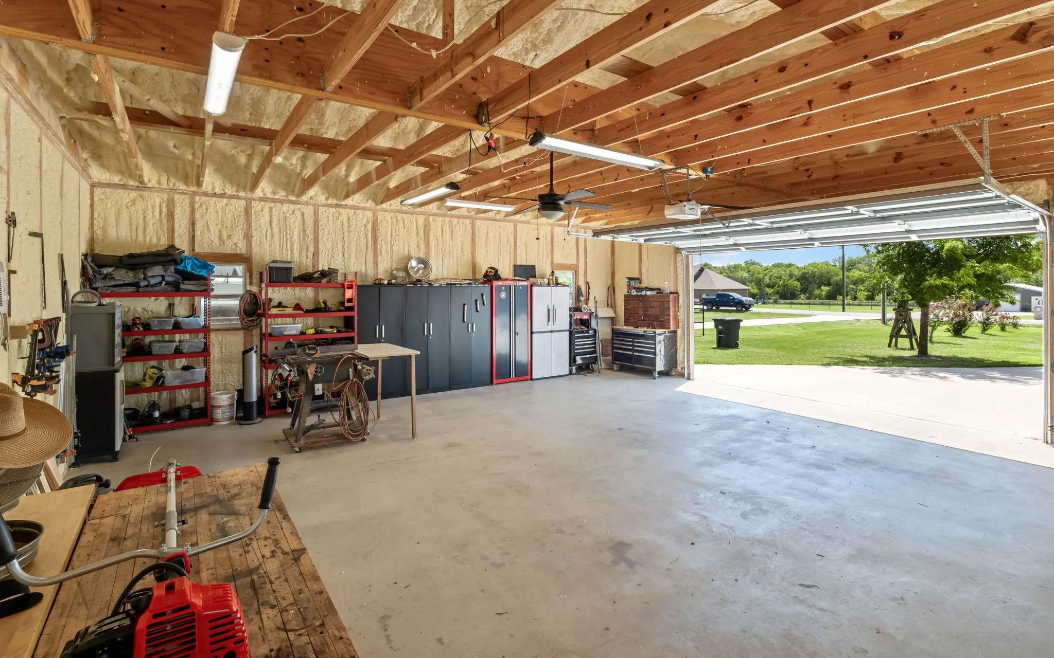 Spacious garage featuring exposed wood beam ceilings, spray foam insulation, and a concrete floor