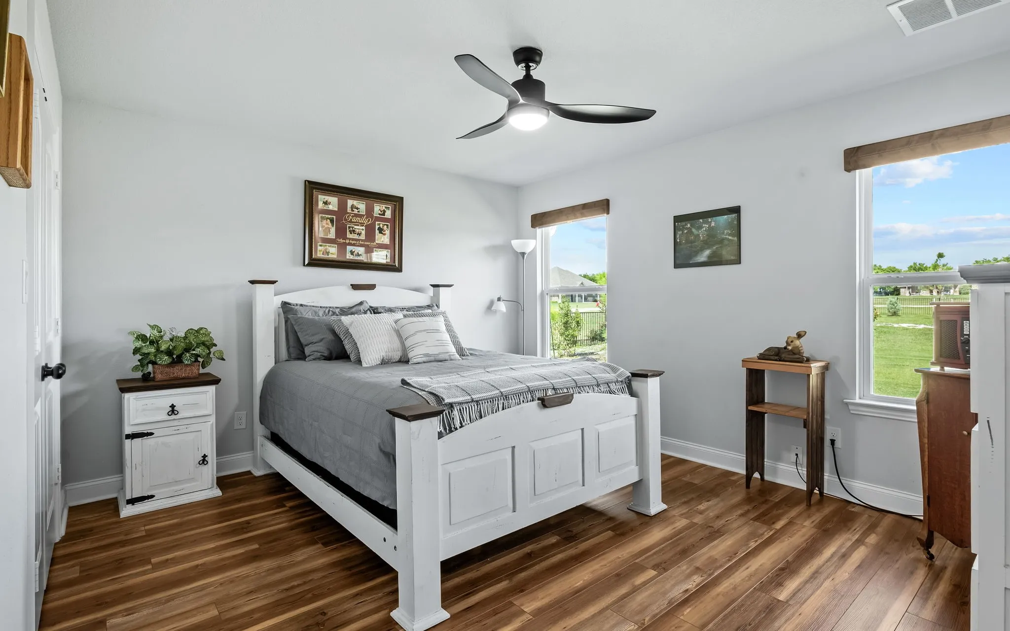 Bright bedroom featuring wood-finish flooring, two large windows with natural light