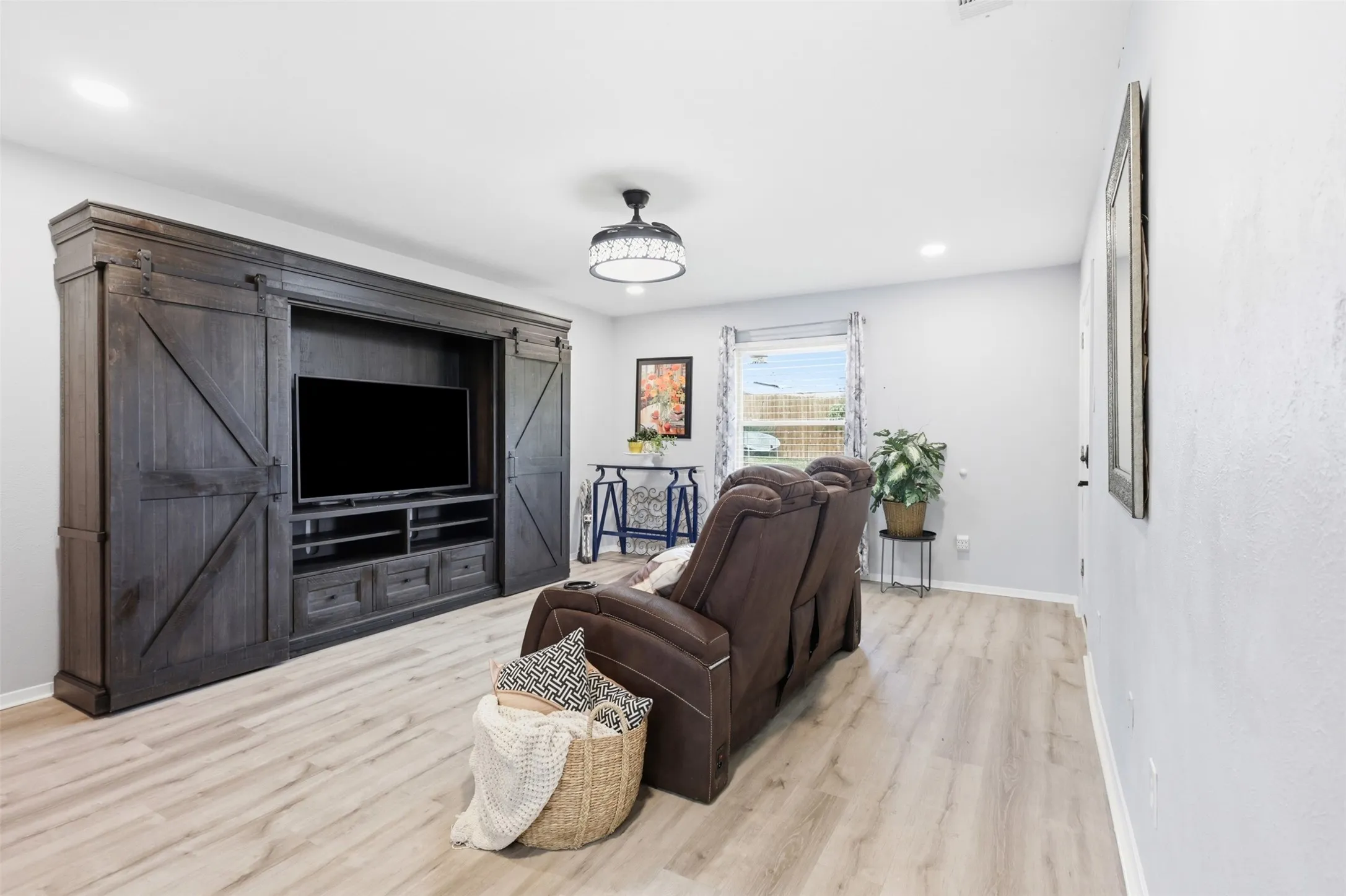 Spacious living area featuring a built-in entertainment center with sliding barn doors, light wood-finish flooring, recessed lighting, and a ceiling fan with integrated lighting