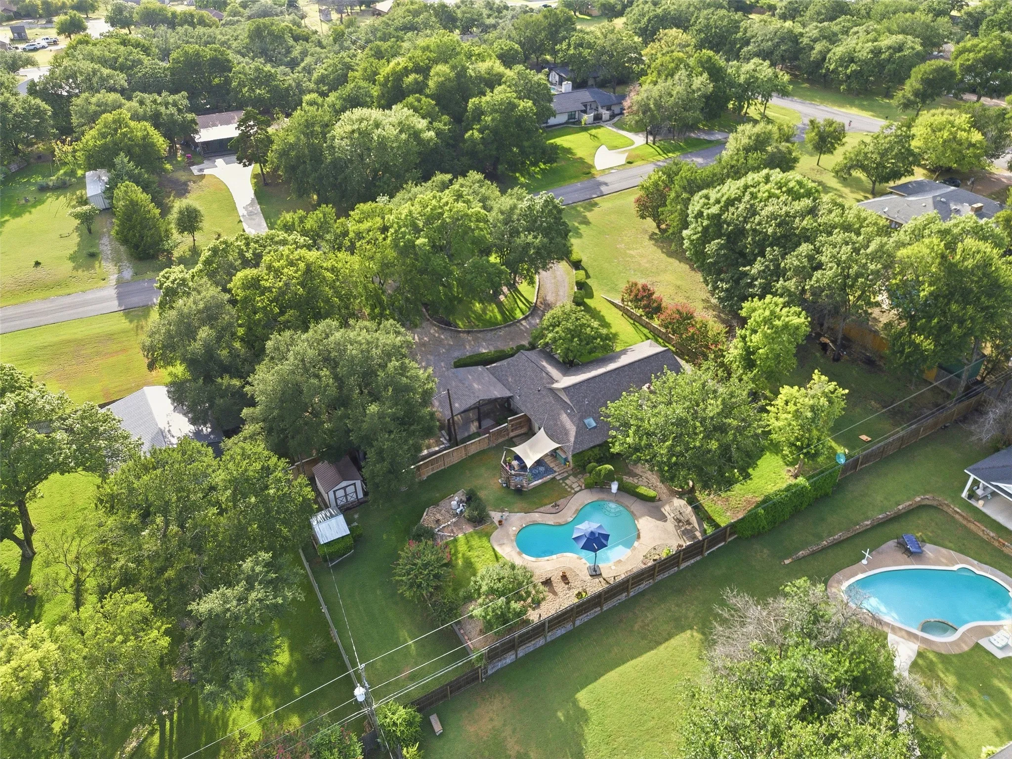 Spacious property featuring a large swimming pool with surrounding patio, a dedicated outdoor seating area with canopy, and mature trees providing ample shade