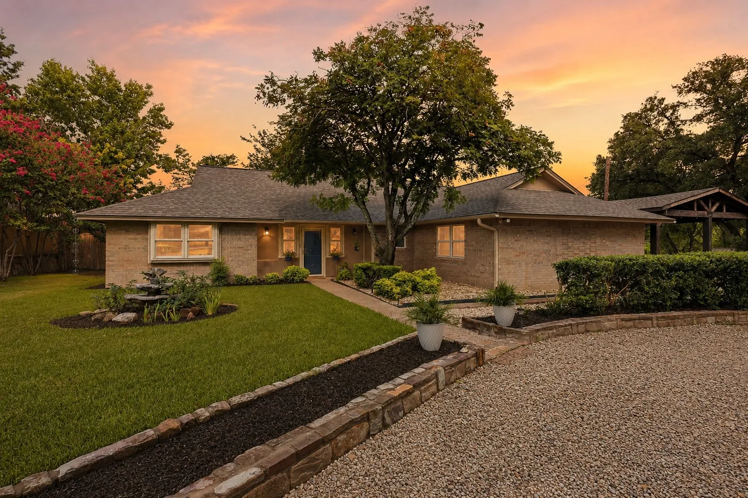 Brick exterior featuring a dark asphalt shingle roof, established landscaping, a gravel driveway, and a covered portico