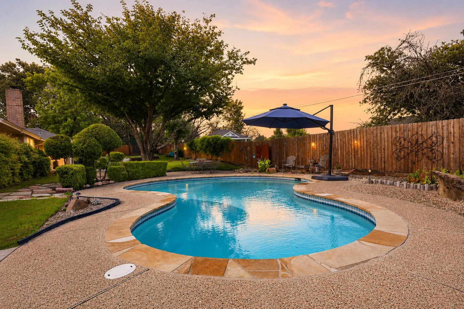Curved swimming pool featuring a textured aggregate deck and coping stones
