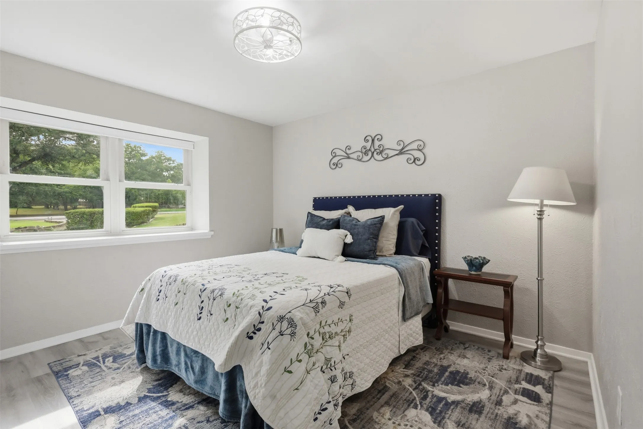 Bright room featuring a large window, light grey walls, wood-finish flooring, and an ornate ceiling light fixture