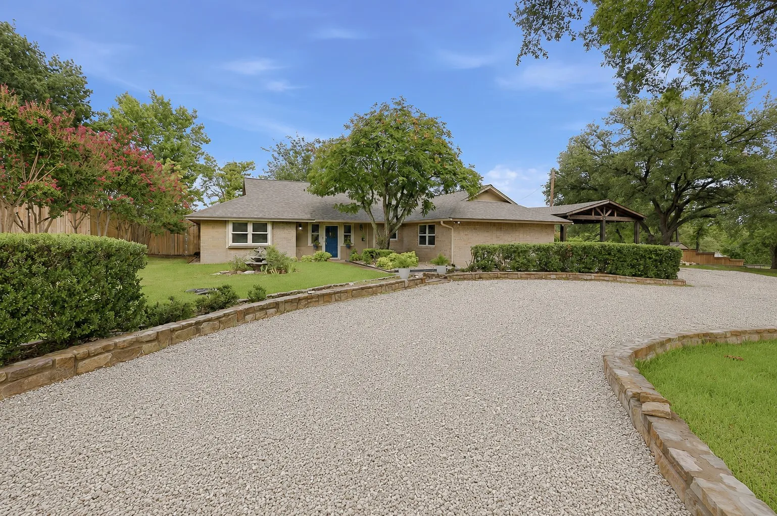 Brick exterior residence featuring a gravel driveway with stone borders, manicured hedges, and mature trees