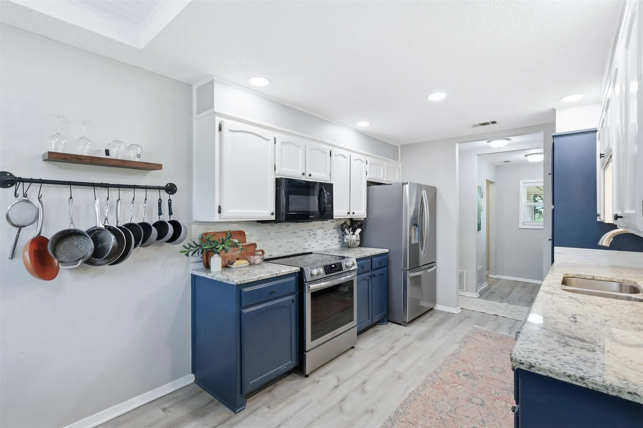Kitchen featuring two-tone cabinetry with white upper and blue lower cabinets, stainless steel appliances, speckled stone countertops, and light wood-finish flooring