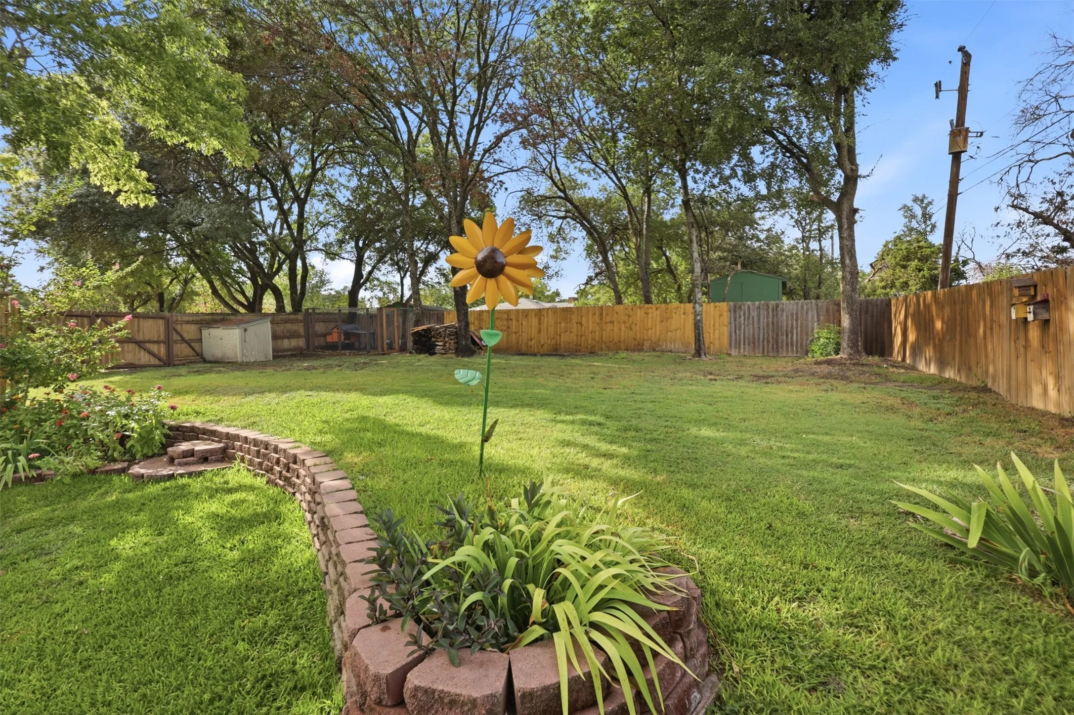 Expansive lawn area featuring a decorative brick-style retaining wall, mature trees, wood fencing, and a storage shed