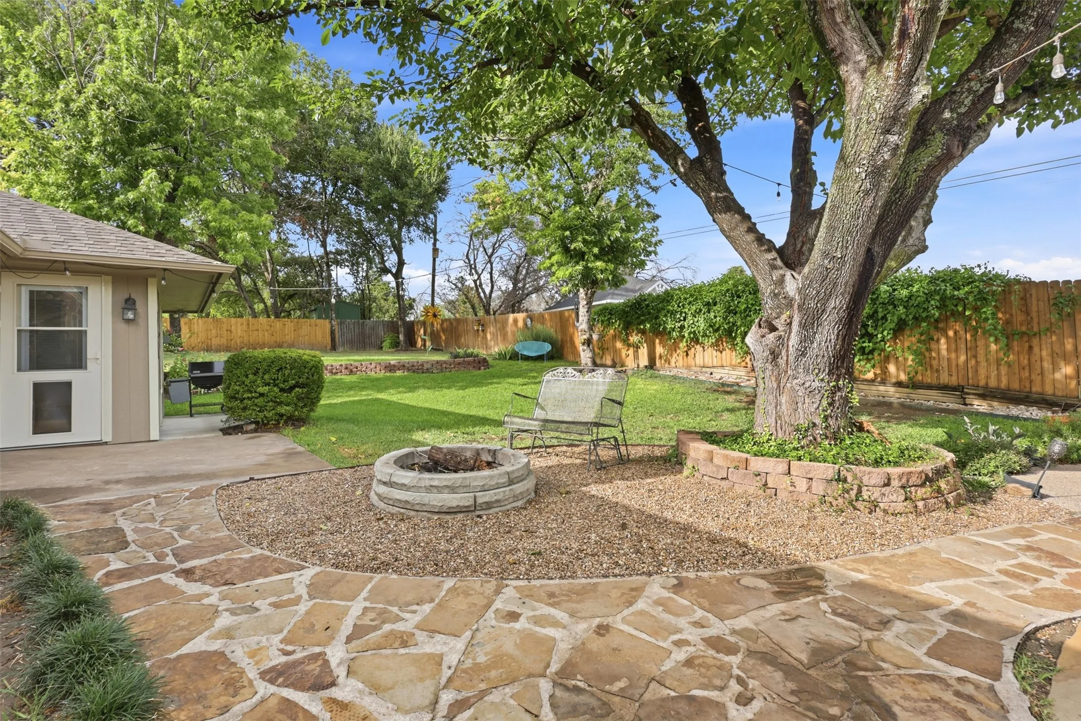 Expansive backyard featuring a natural stone patio, gravel landscaping, and a built-in fire pit with stone surround