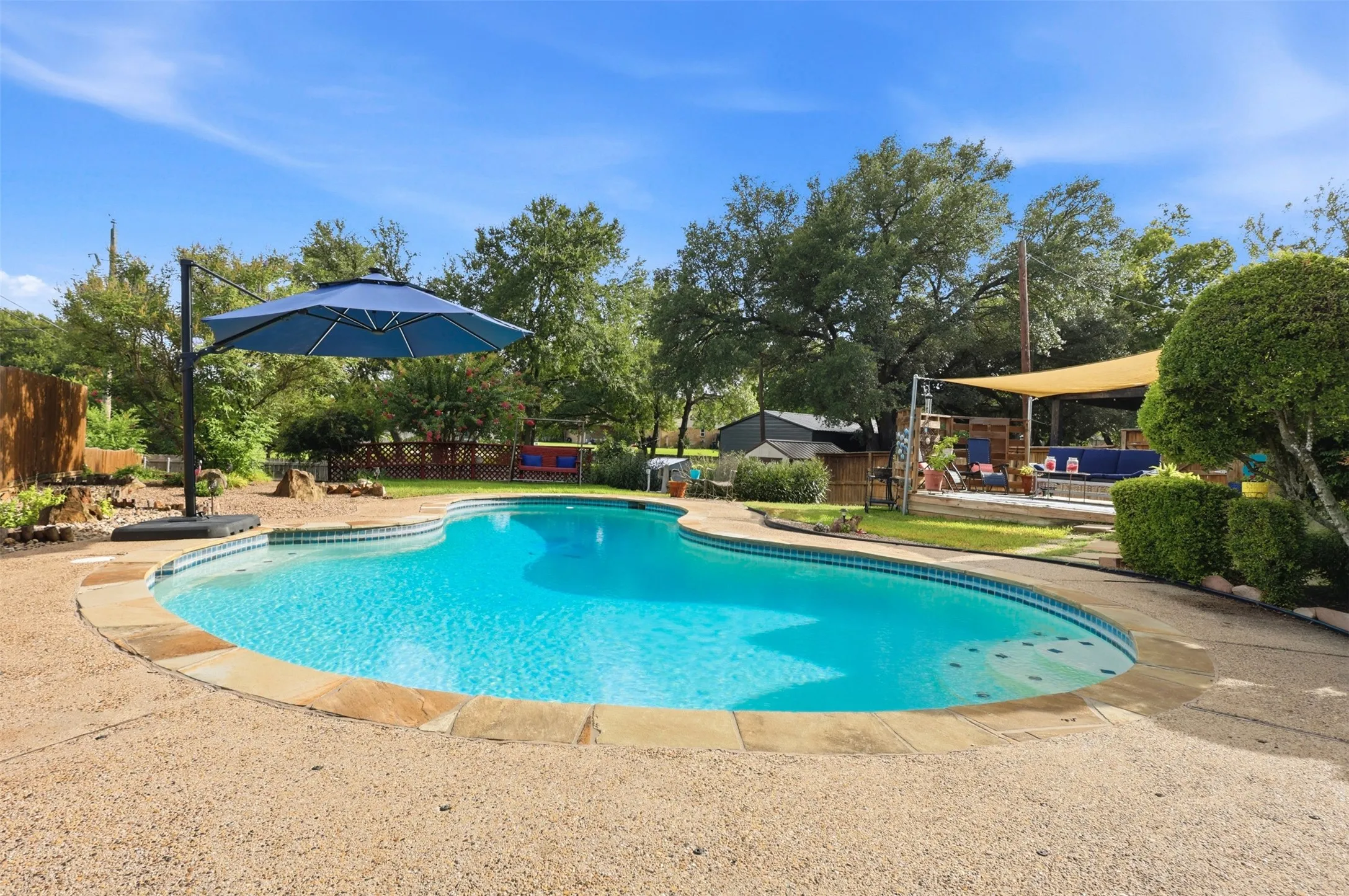 Curved swimming pool with stone coping and exposed aggregate decking