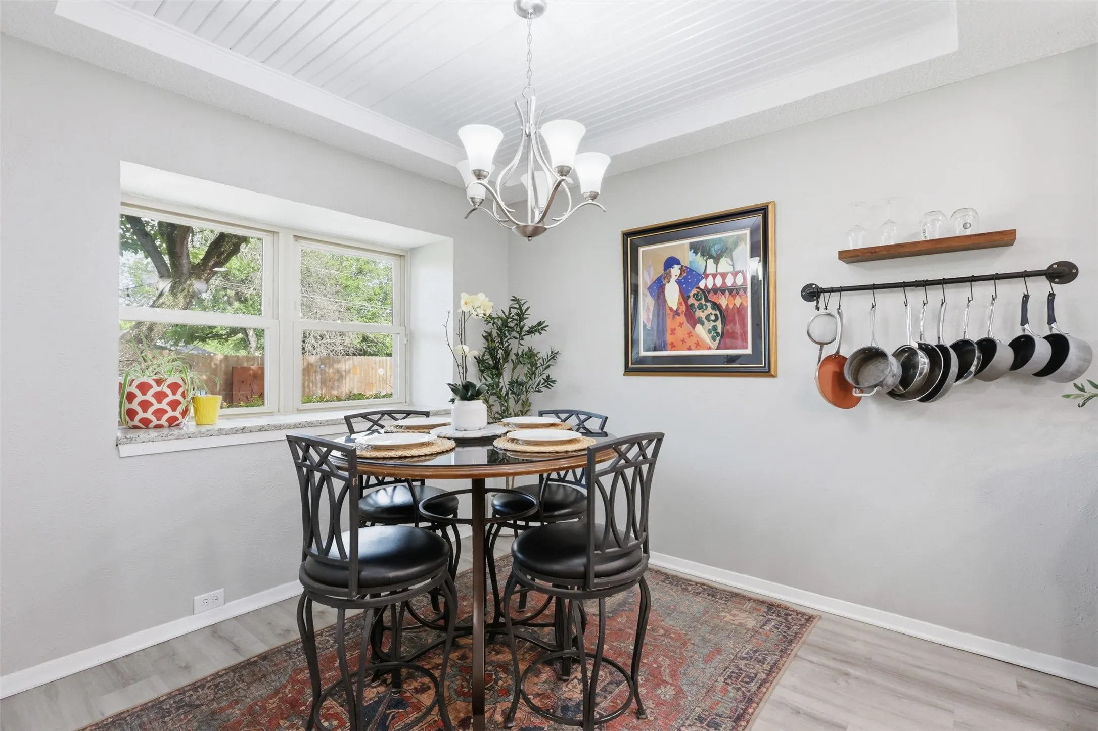 Dining area featuring light wood-finish flooring, a tray ceiling with white paneling, and a contemporary chandelier