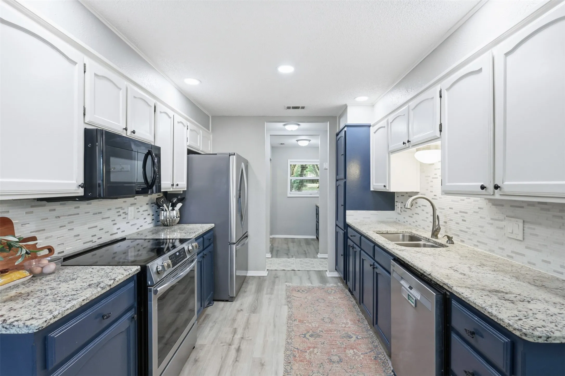 Galley kitchen featuring dual-tone cabinetry, light granite-finish countertops, and a full suite of stainless steel appliances