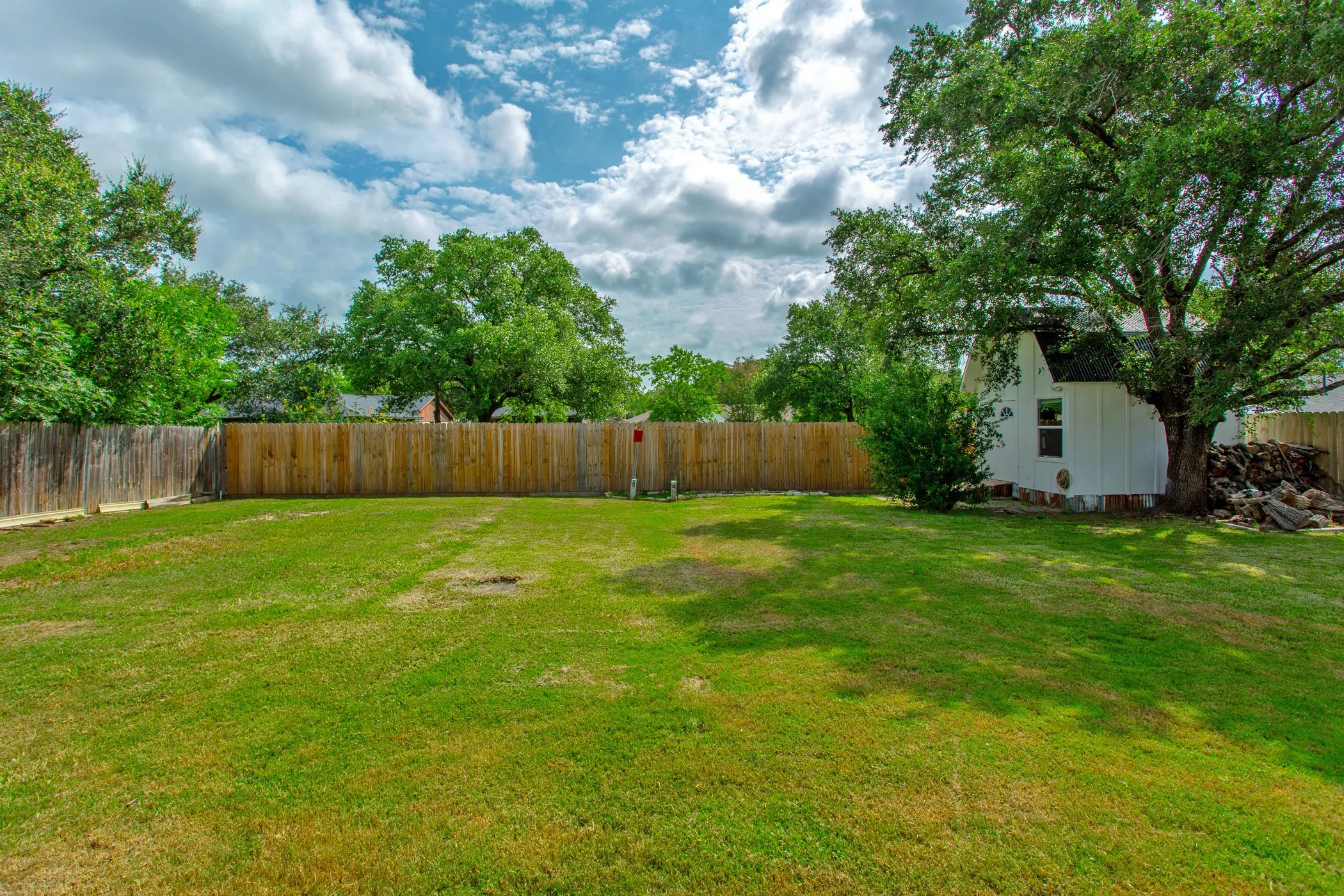 Expansive backyard featuring a lush lawn, privacy fencing, and mature trees