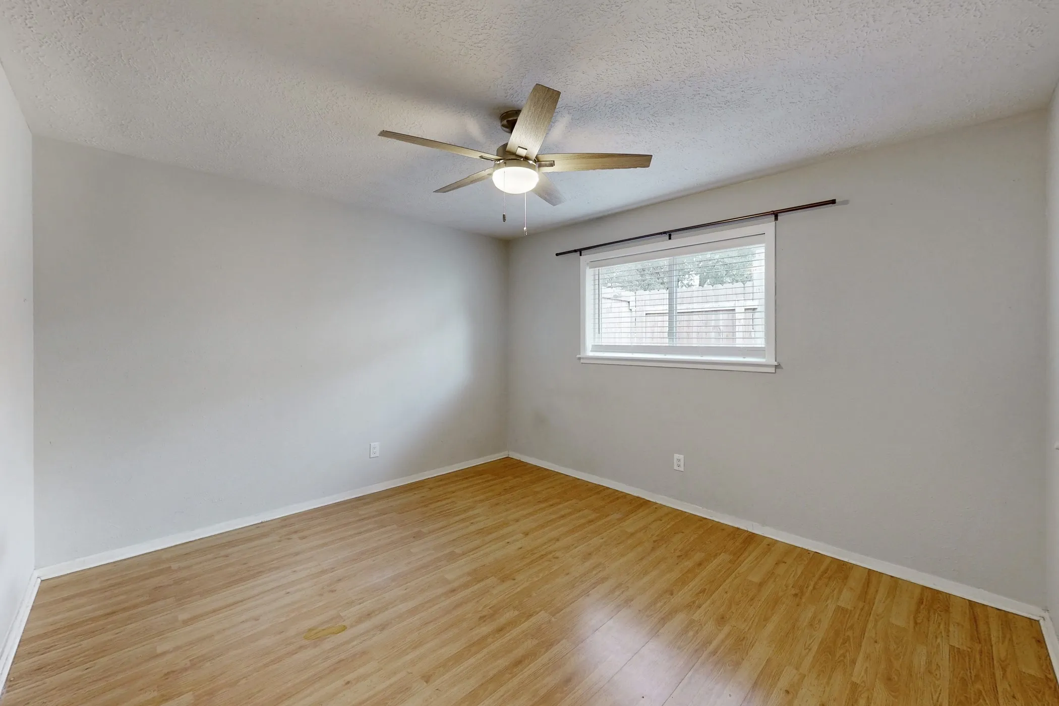 Bright room featuring wood-finish flooring, light gray walls, a ceiling fan with integrated lighting, and a window with blinds