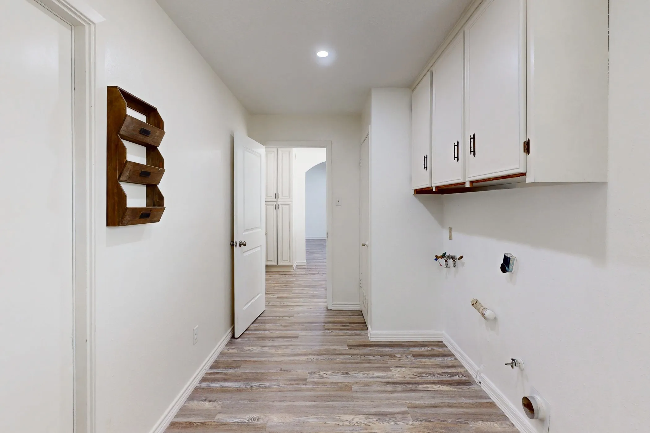 Dedicated laundry space featuring multiple wall-mounted white cabinets with dark hardware, plumbing hookups for appliances, and wood-finish flooring