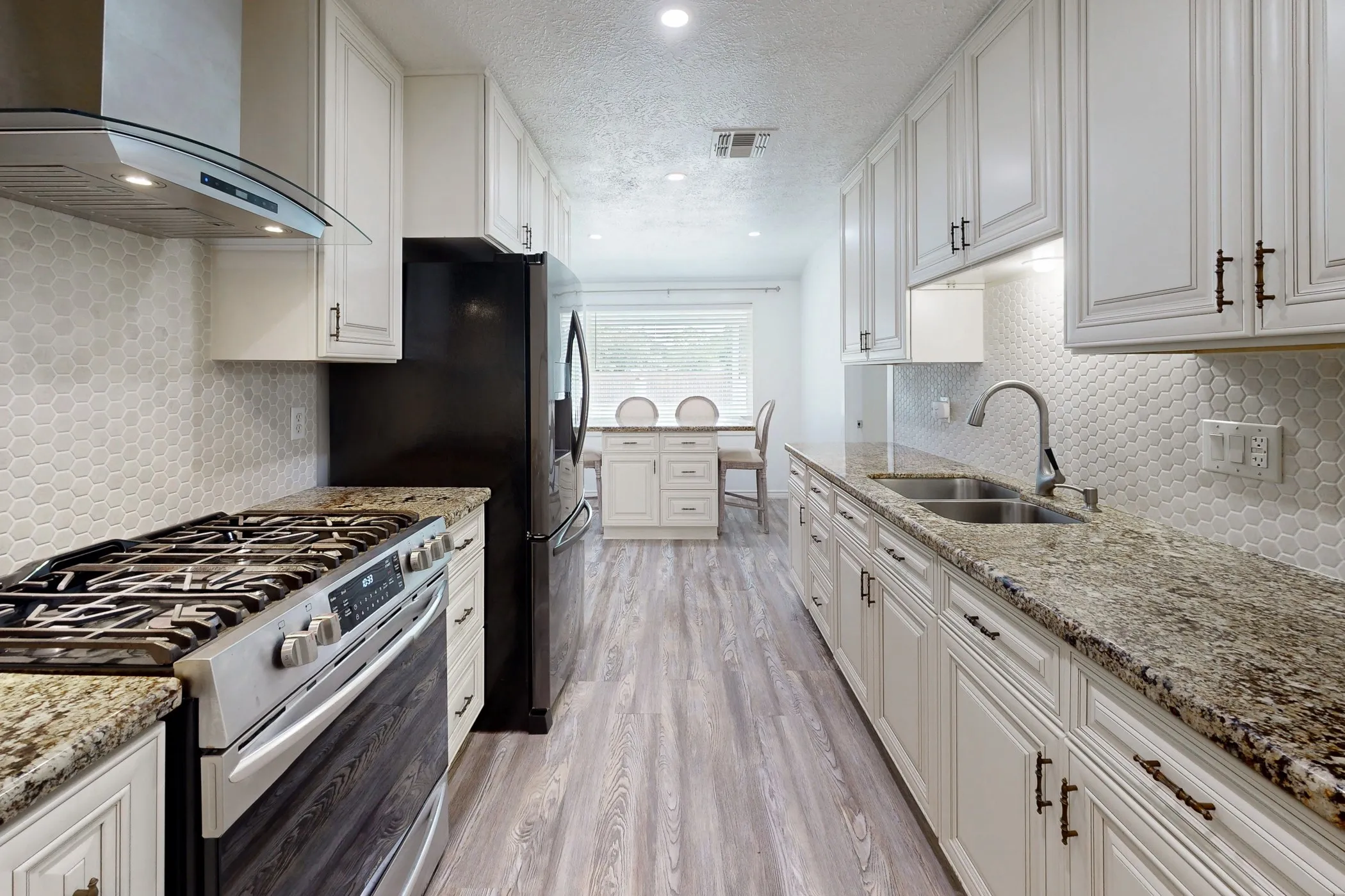 Galley kitchen featuring white cabinetry, granite countertops, a gas range with a stainless steel vent hood, and a dual basin sink