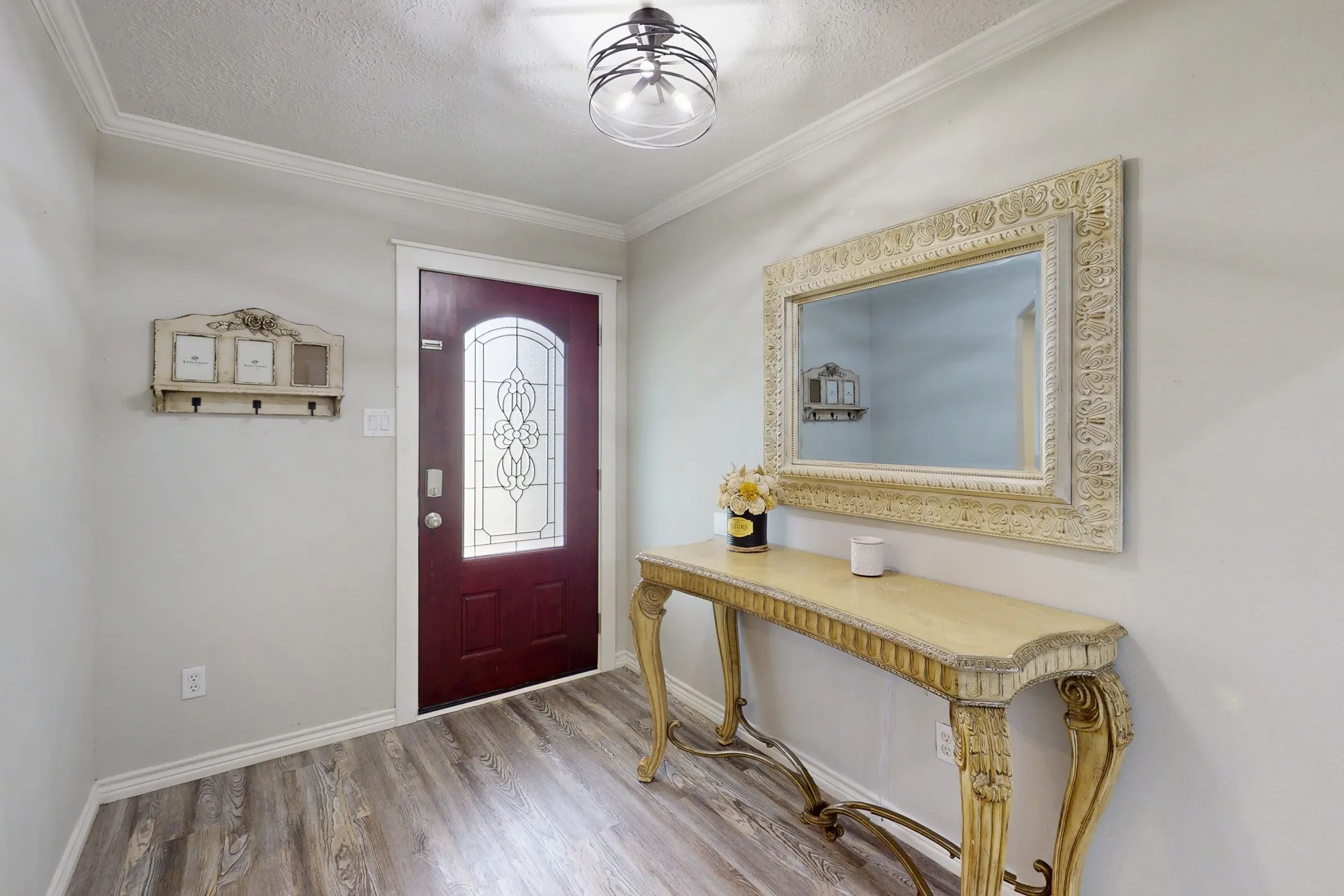 Entryway featuring wood-finish flooring, a burgundy door with decorative glass inserts, and crown molding