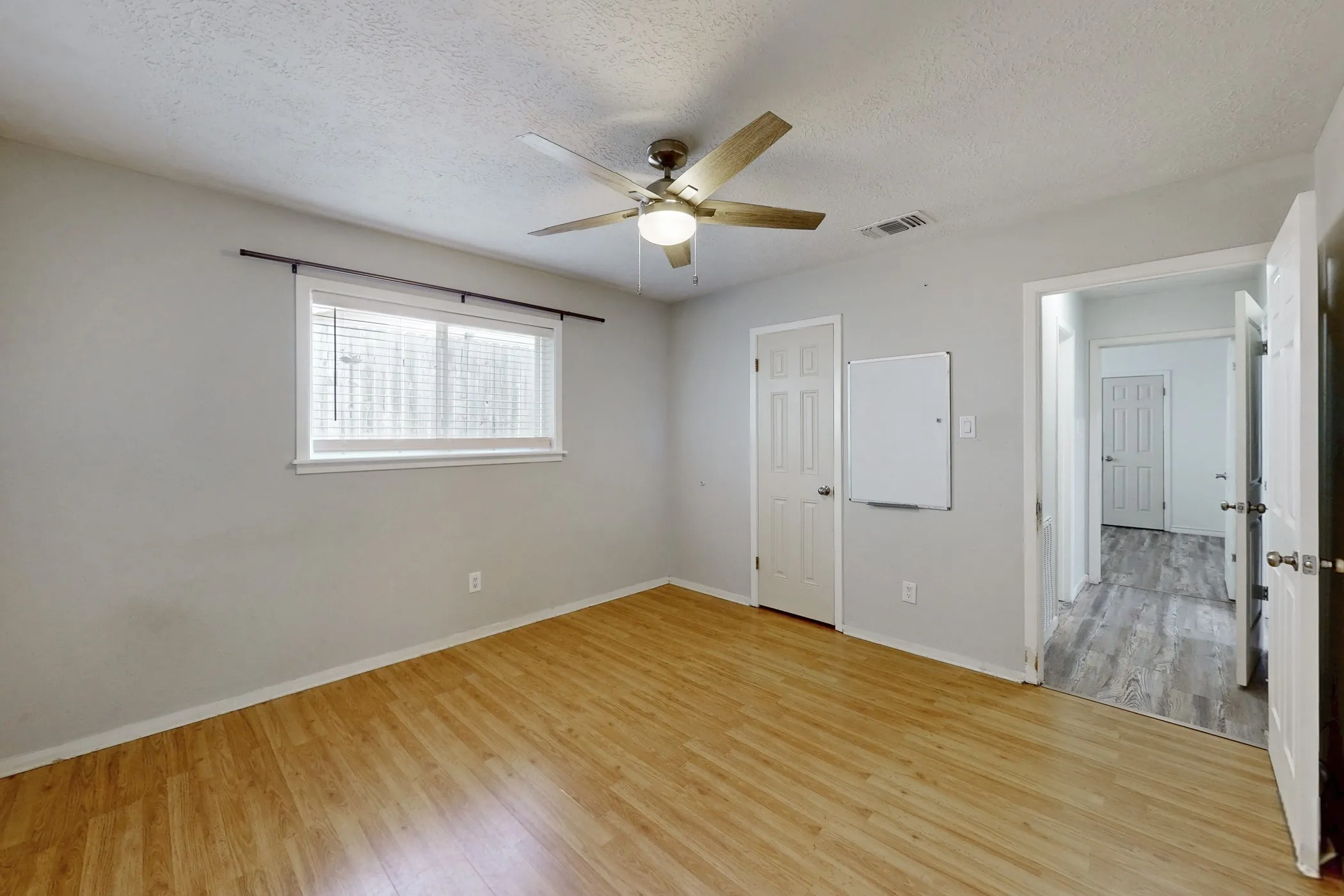 Room featuring wood-finish flooring, a ceiling fan, and a window with blinds