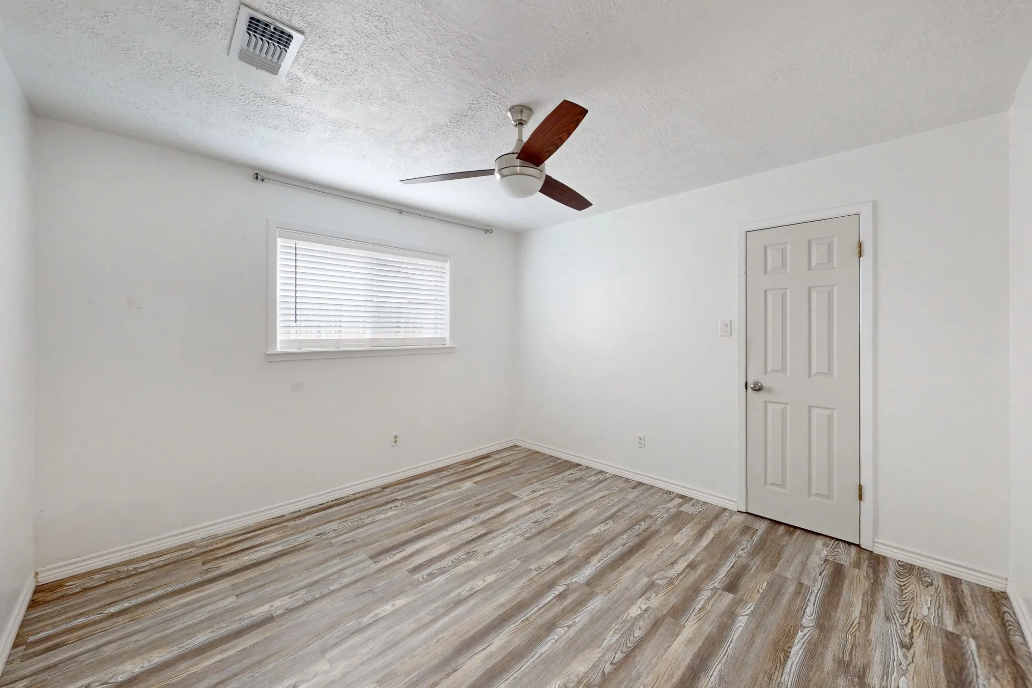 Spacious room with wood-finish flooring and a white paneled door