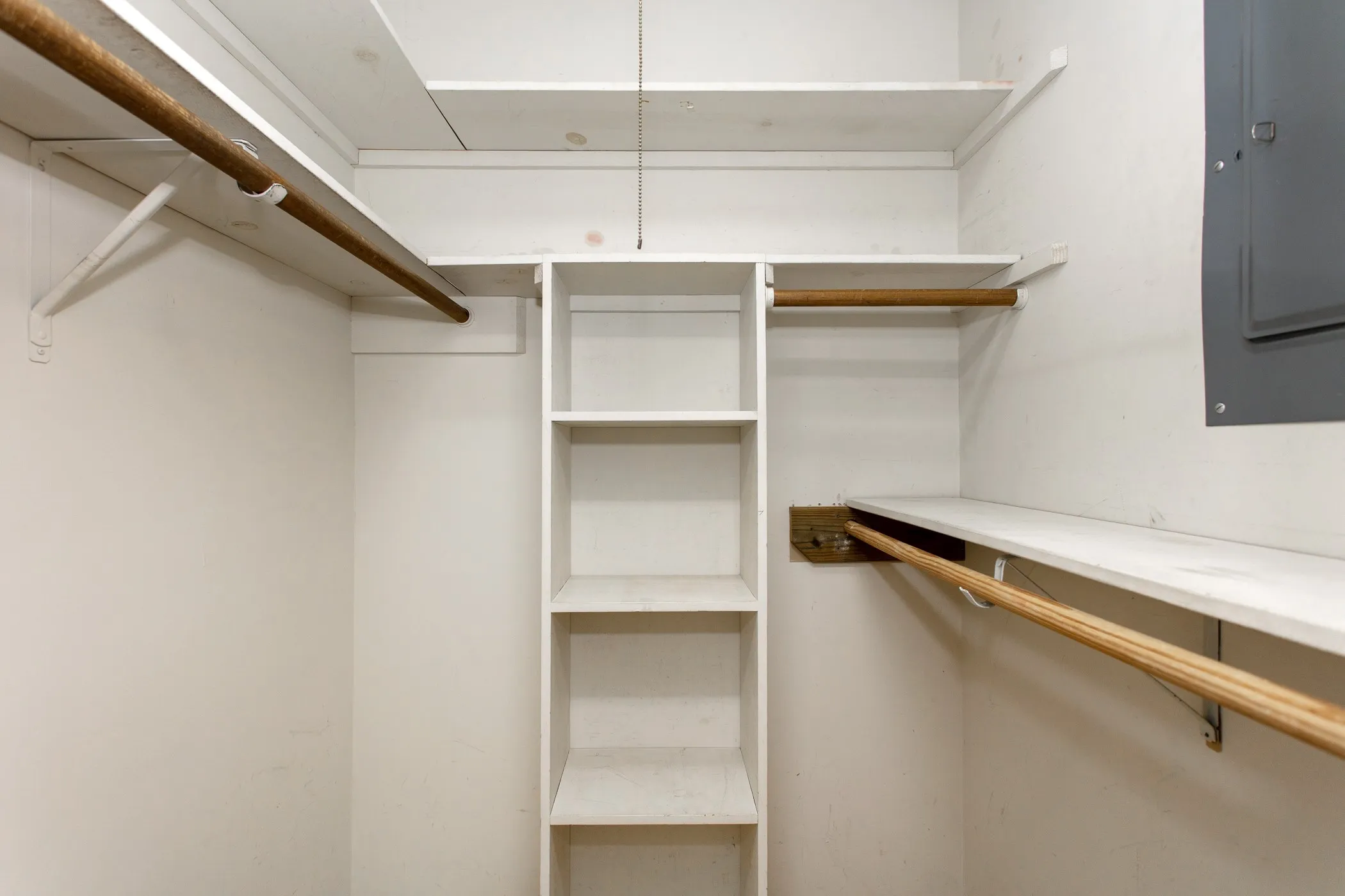 Walk-in closet featuring white built-in shelving, two levels of hanging rods, and an additional single hanging rod