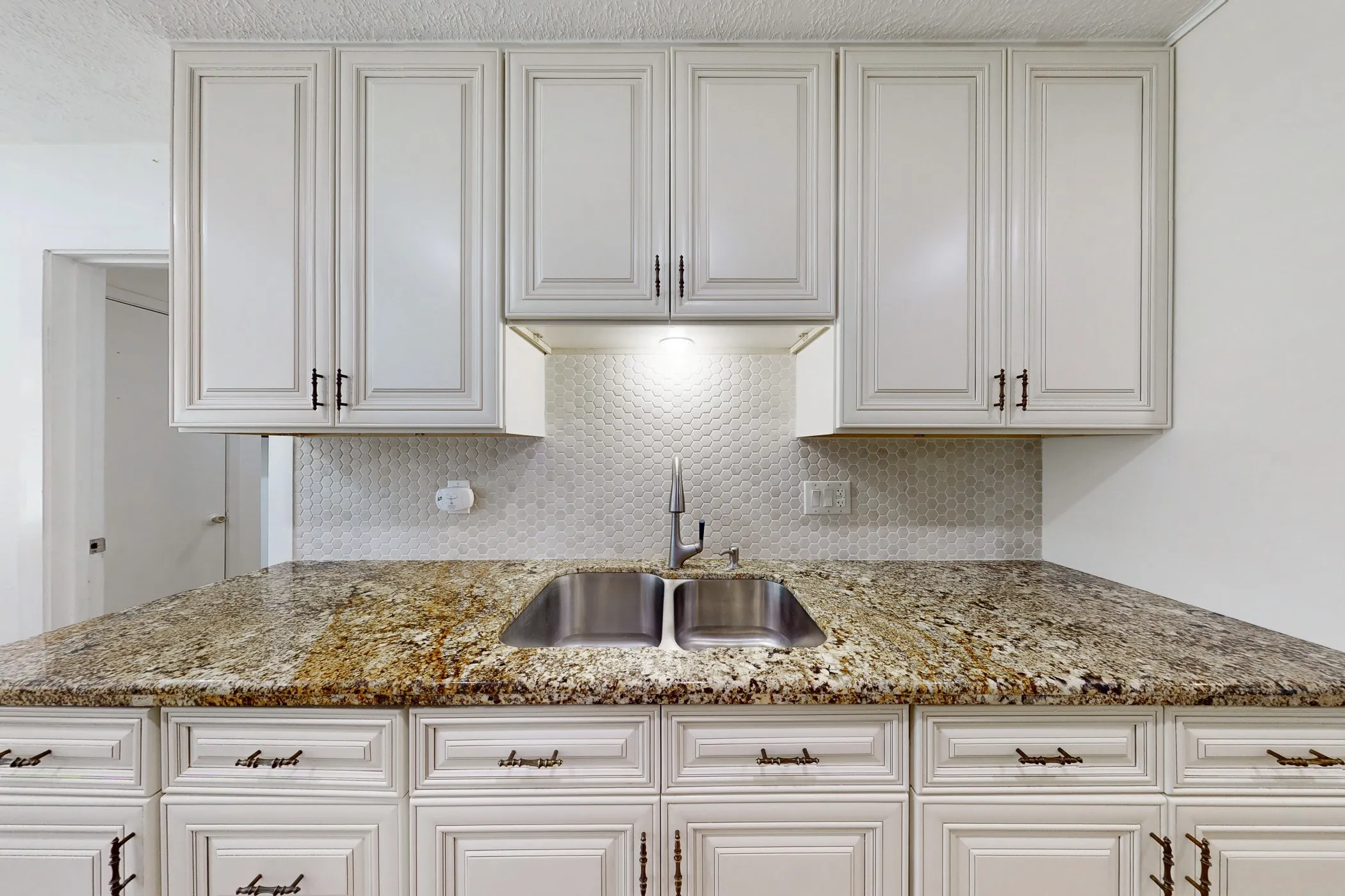 Kitchen featuring light-toned cabinetry with dark hardware, a double basin stainless steel sink, and a speckled countertop