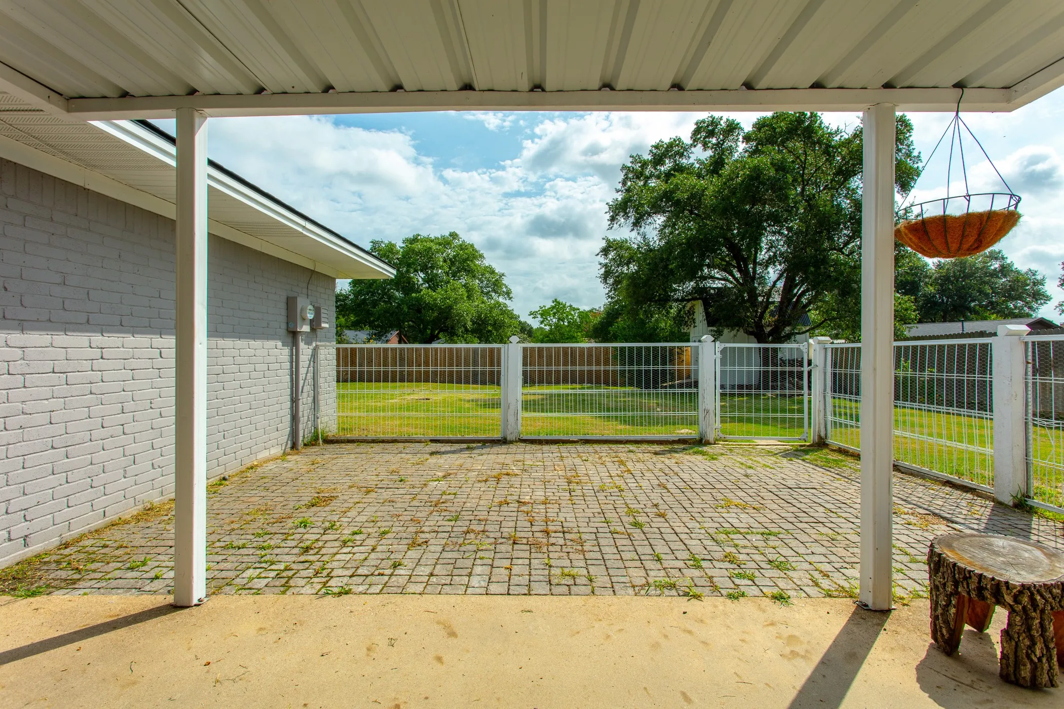 Covered patio with a corrugated metal roof, extending to a paved brick courtyard