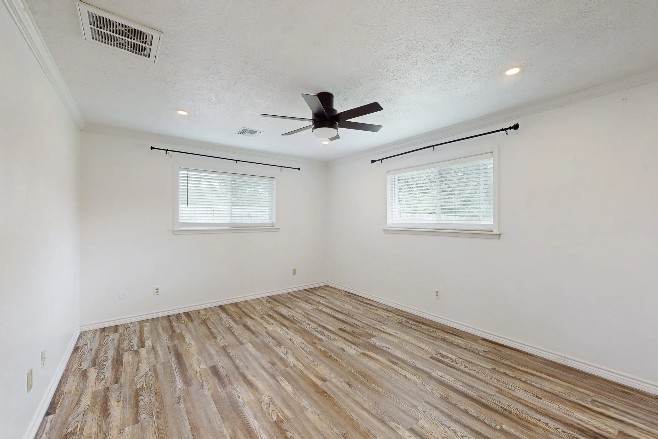Spacious room featuring wood-finish flooring, white walls, and crown molding