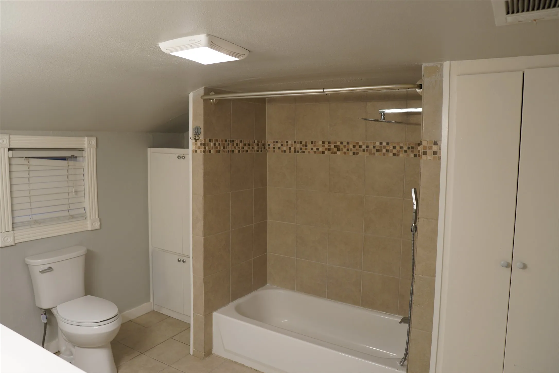 Bathroom featuring a shower-over-tub combination with large format tile surround and decorative mosaic accent