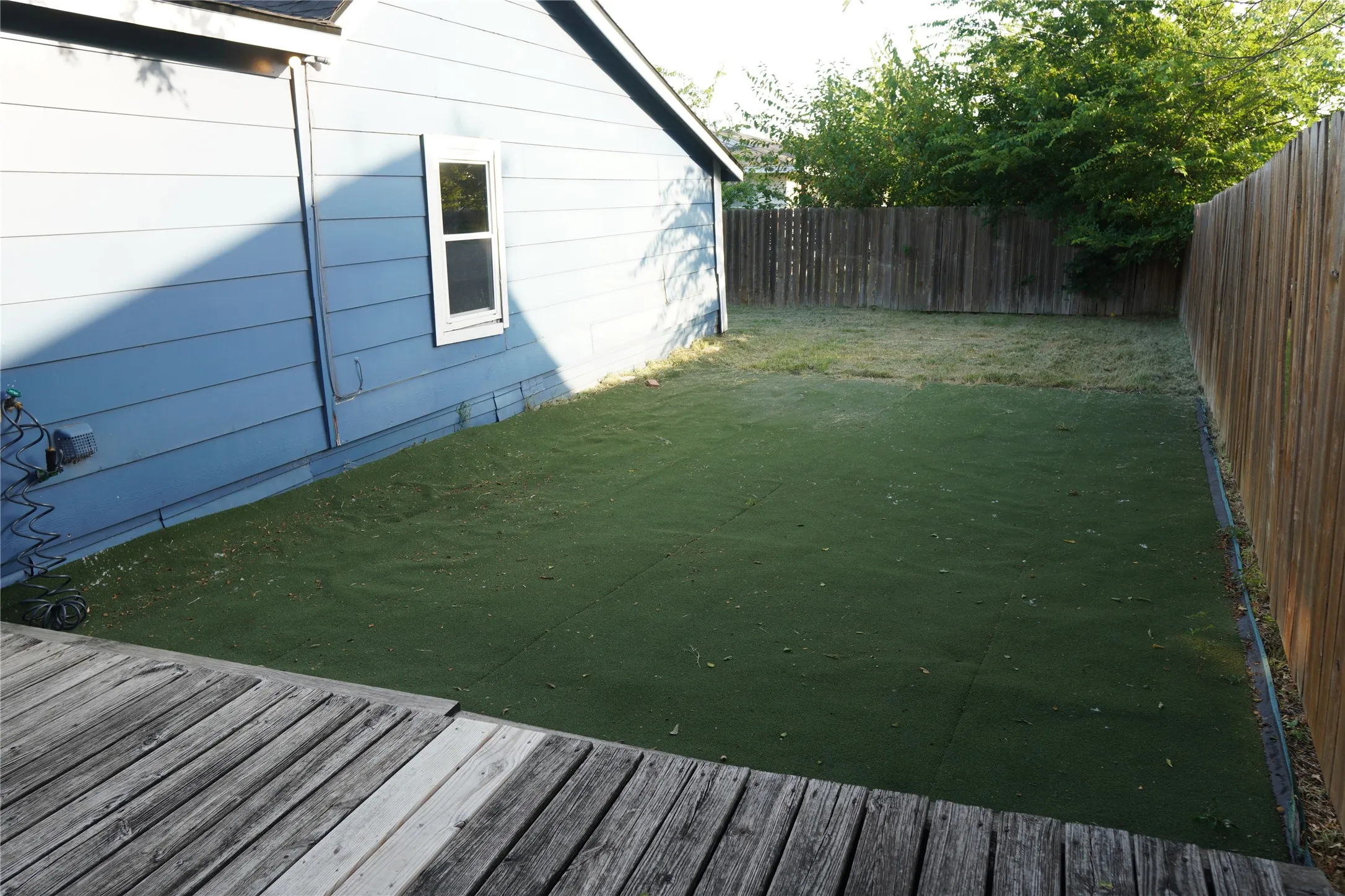 Backyard featuring a wooden deck, artificial turf section, natural grass area, and a wood privacy fence