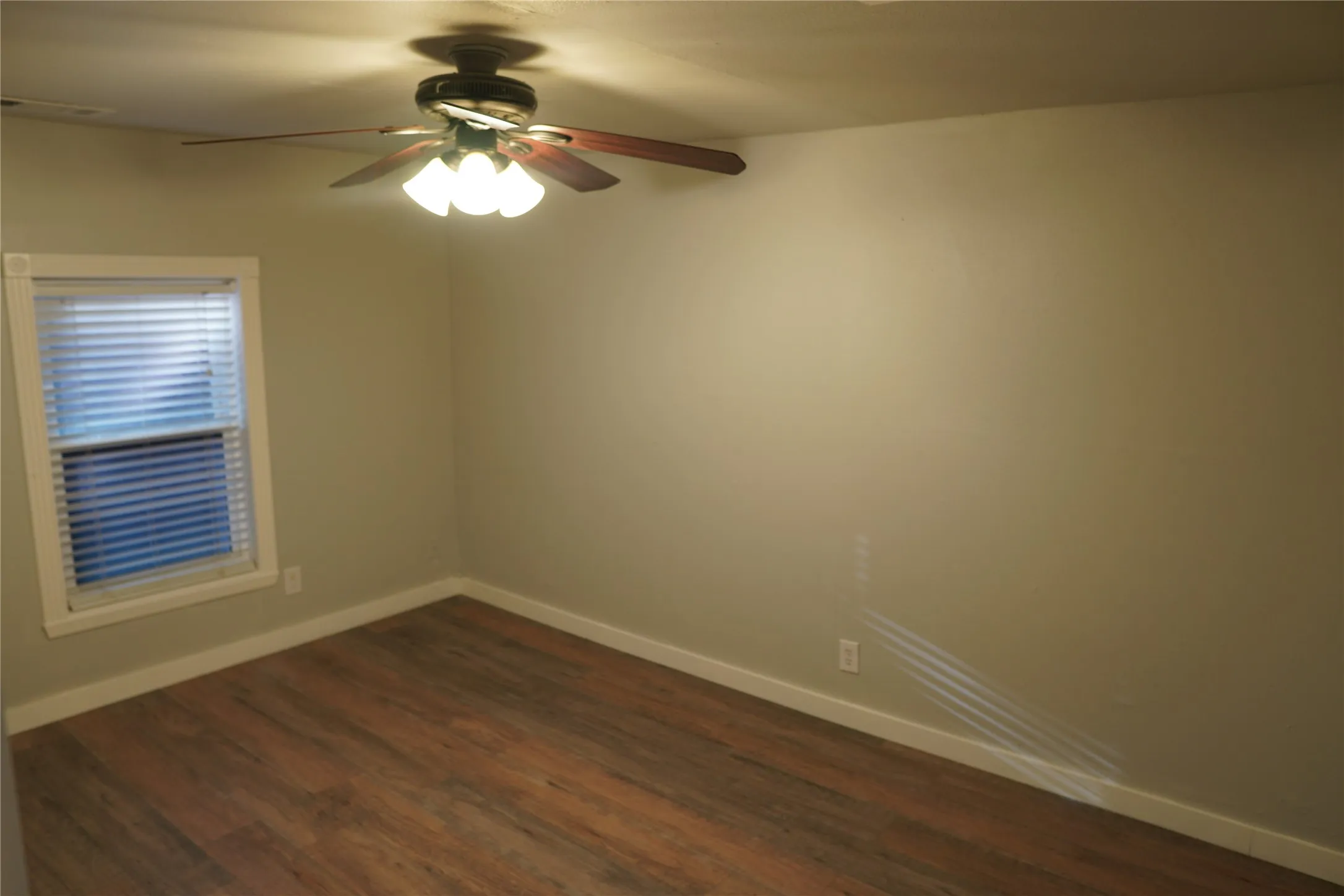 Spacious bedroom featuring wood-finish flooring, a ceiling fan with integrated lighting, a window with blinds, and neutral wall tones