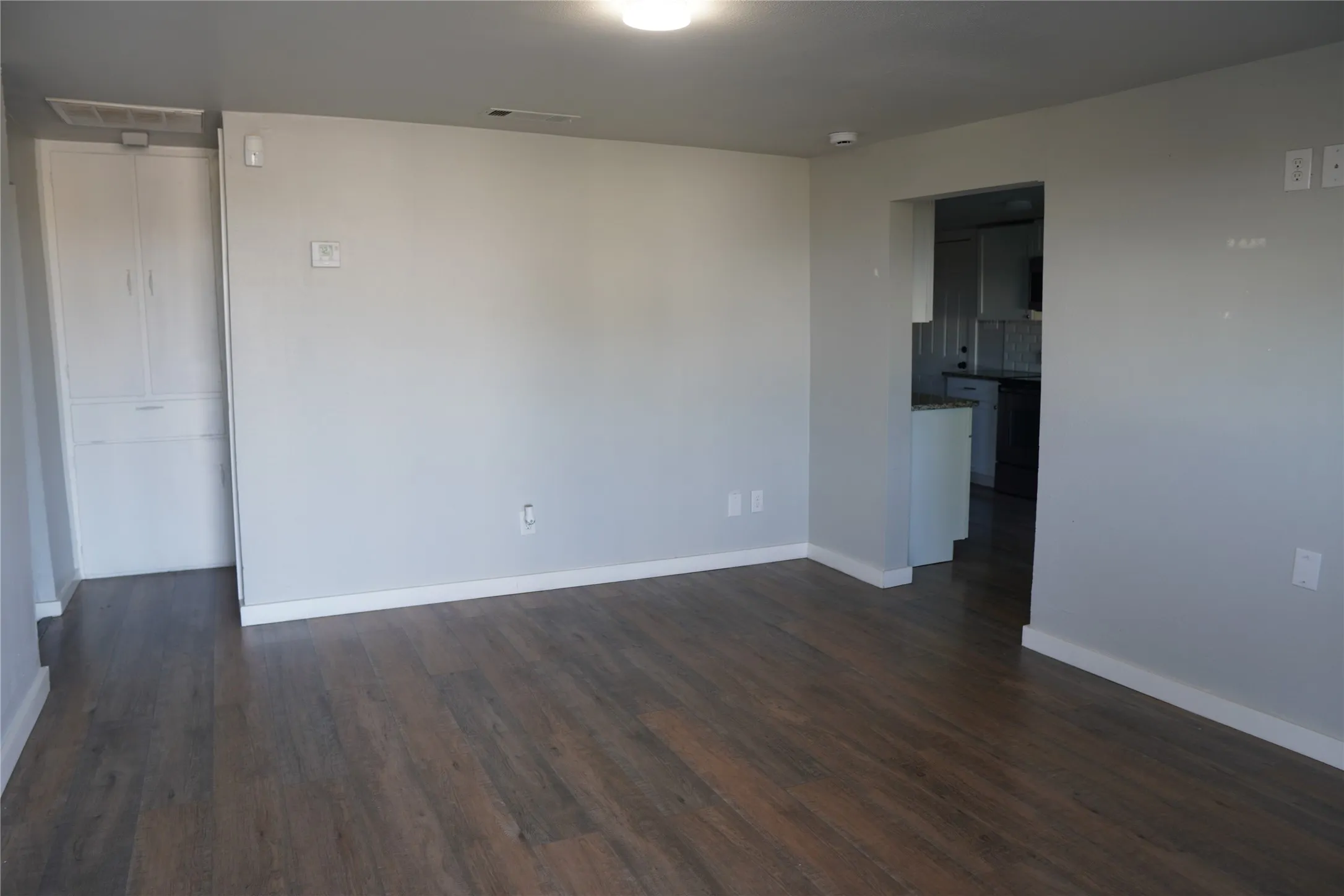 Spacious living room featuring wood-finish flooring, light grey painted walls, white baseboards, and a built-in white cabinet with two doors and a drawer