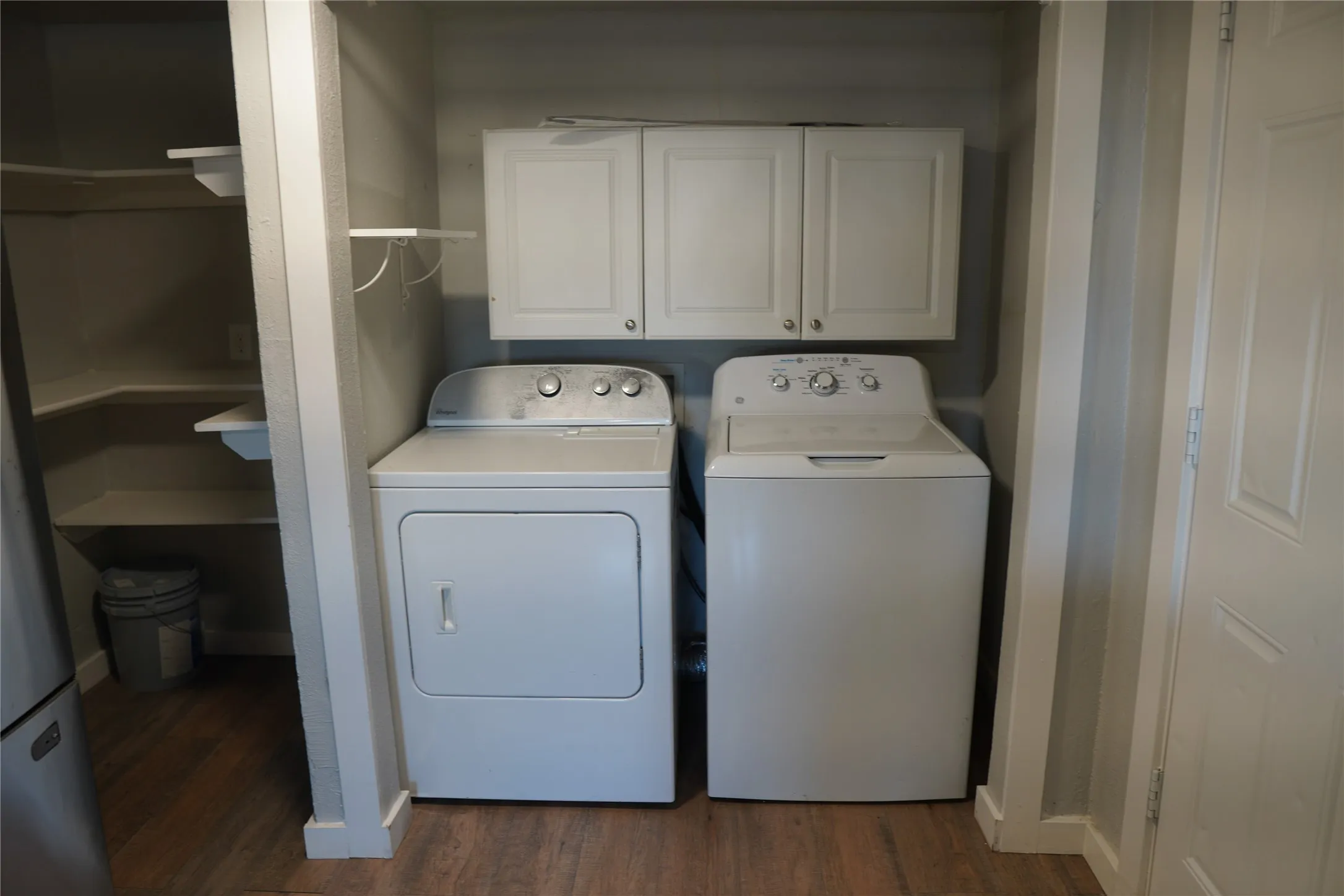 Dedicated laundry area featuring white upper cabinetry, wood-finish flooring, and a recessed pantry with built-in shelving