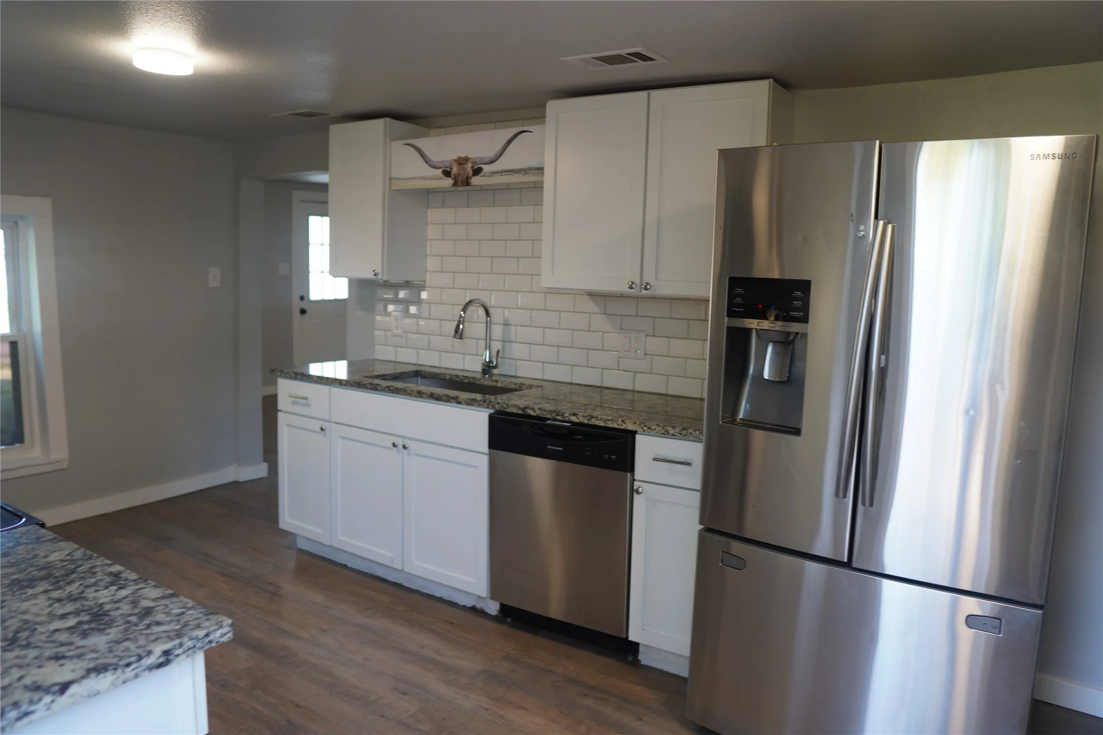 Kitchen featuring white cabinetry, granite countertops, subway tile backsplash, stainless steel appliances, and wood-finish flooring